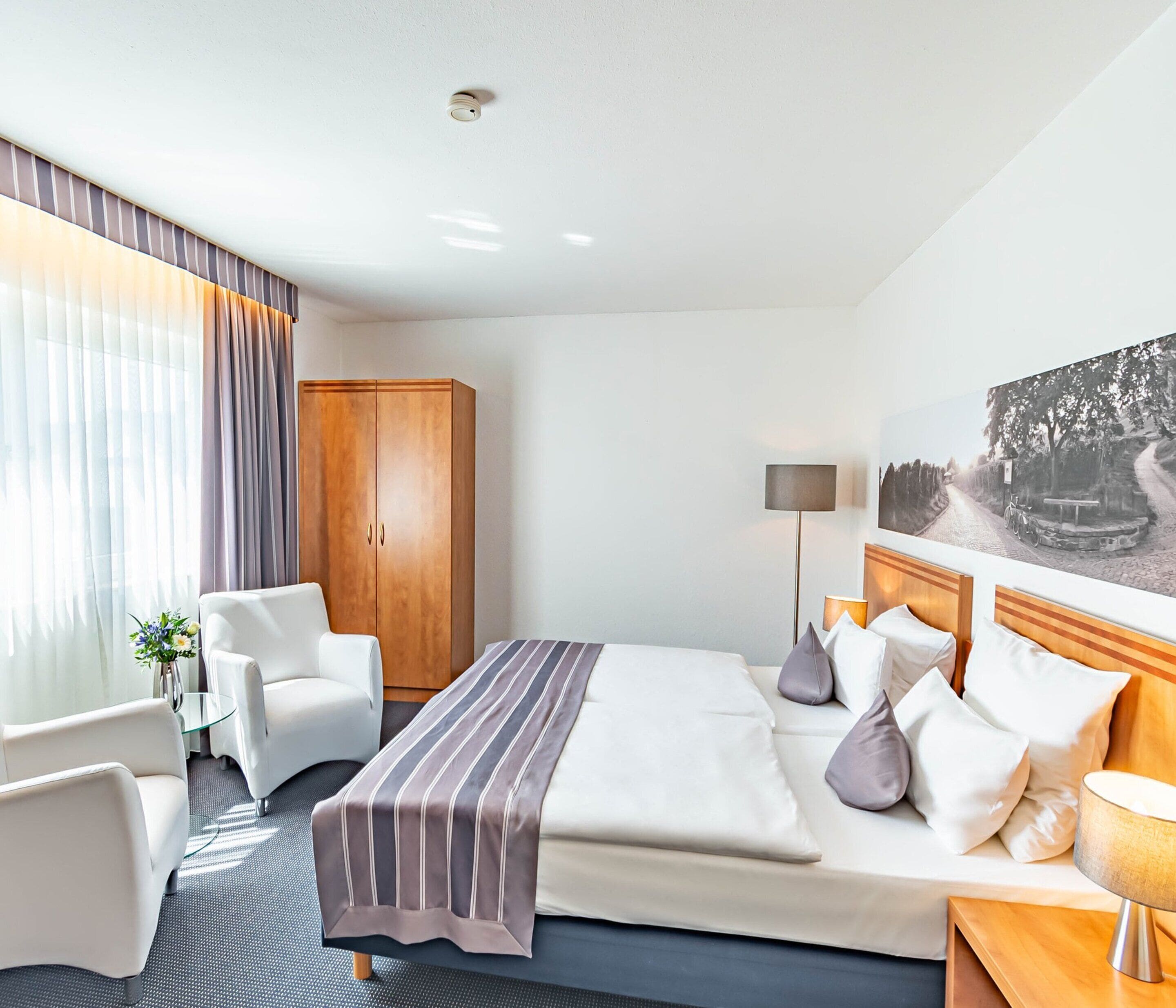 Hotellihuone, jossa on sänky, työpöytä, tuoli, vaatekaappi ja taulu seinällä.