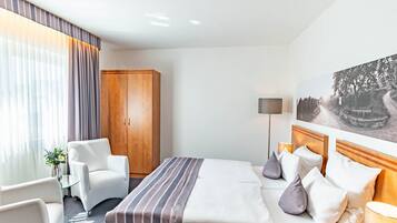 Hotellihuone, jossa on sänky, työpöytä, tuoli, vaatekaappi ja taulu seinällä.