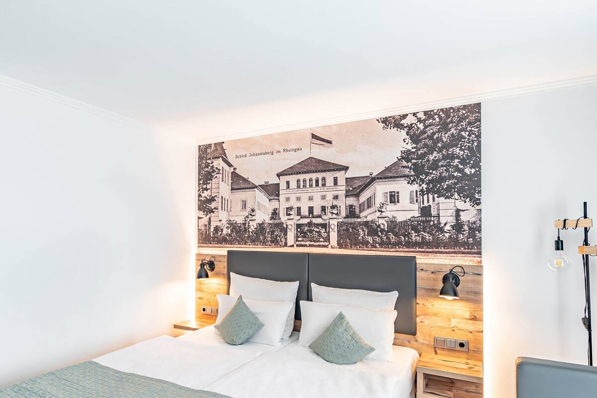 Ein modernes Hotelzimmer mit einem großen Bett, Holz-Nachttischen und einer Stadtlandschaft als Wandbild.