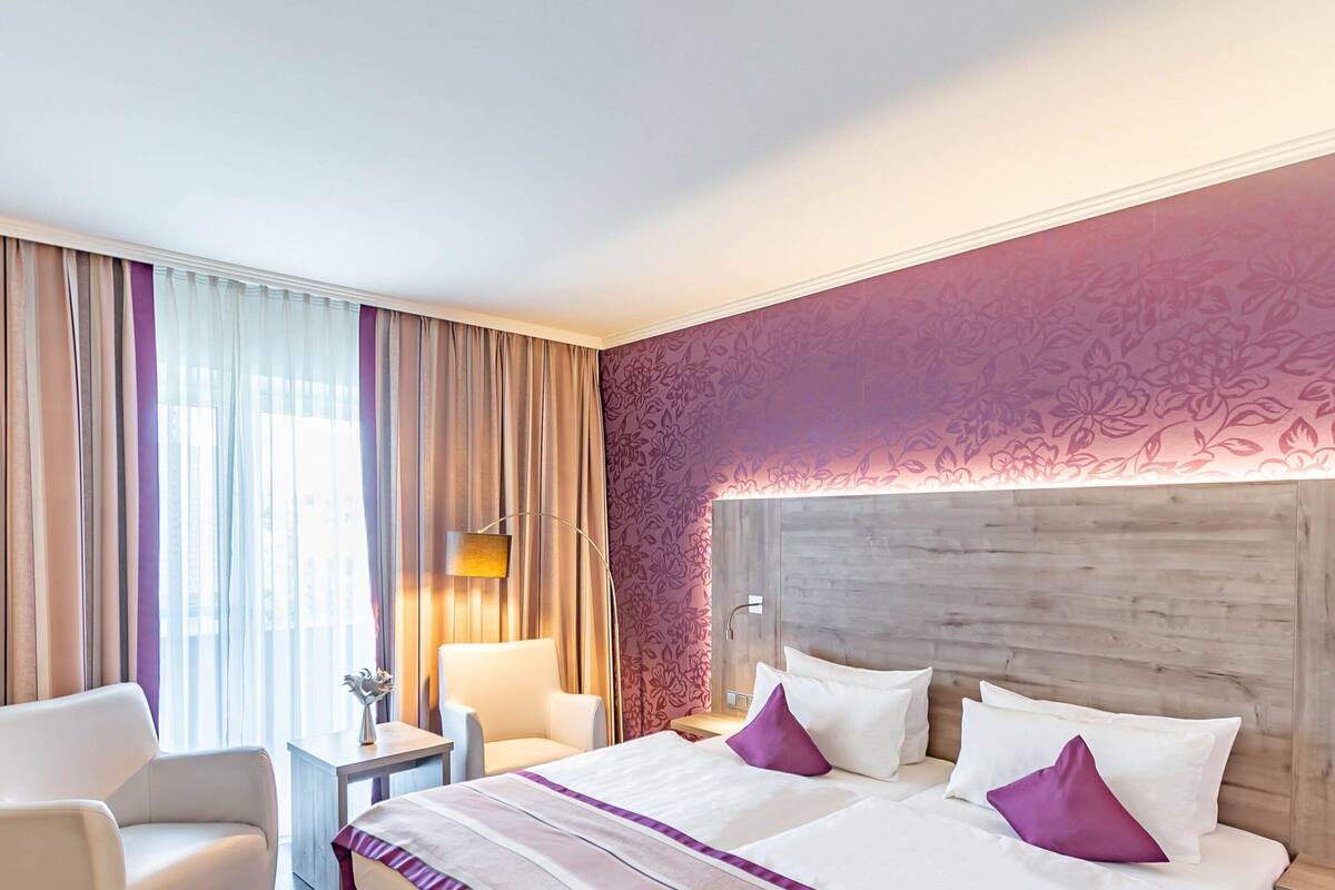 Ein Hotelzimmer mit einem großen Bett, zwei Nachttischen, einem Sessel und einem Schreibtisch.