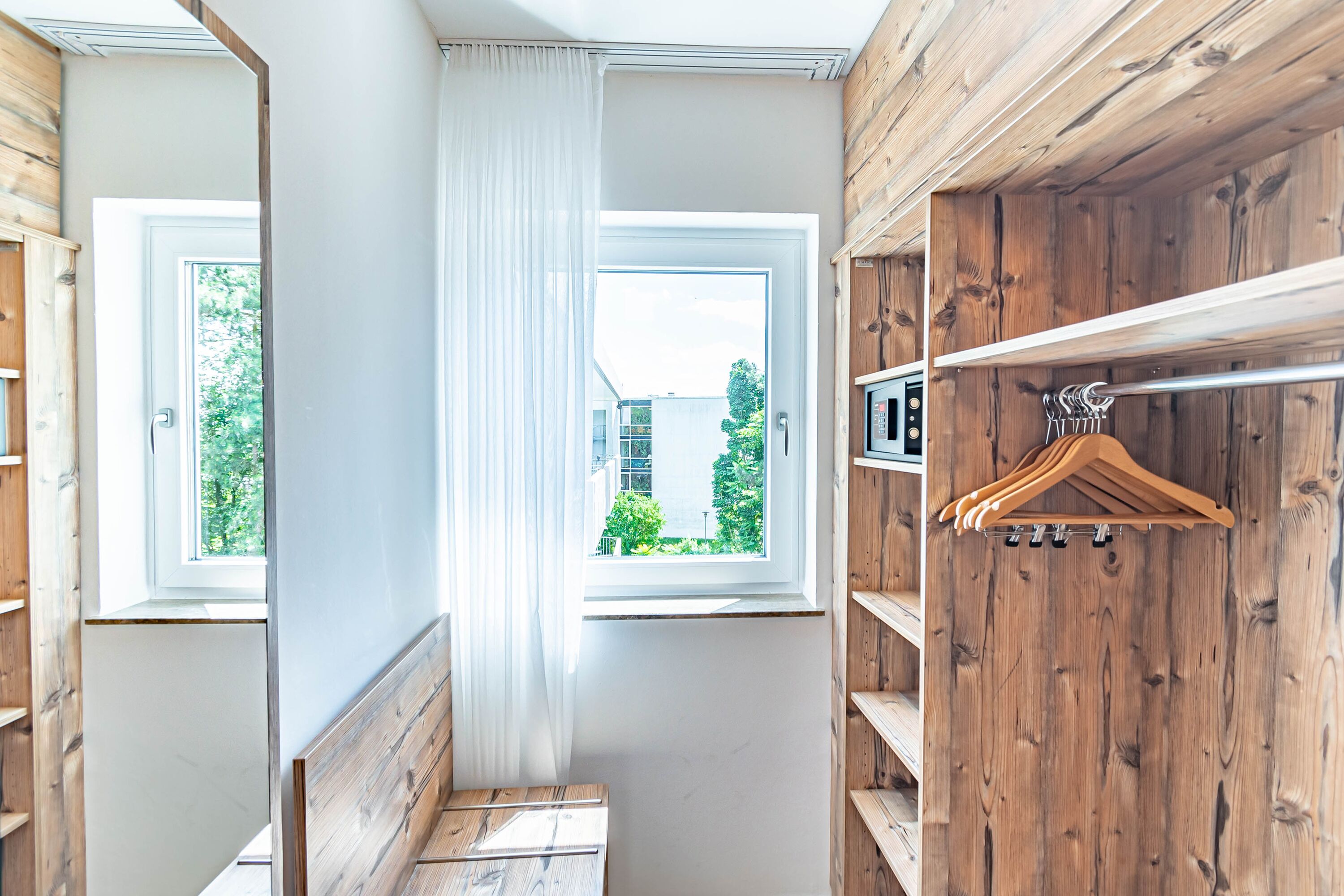 A room with a wooden interior, a window with white curtains, and a coat rack with hangers.
