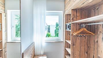 A room with a wooden interior, a window with white curtains, and a coat rack with hangers.