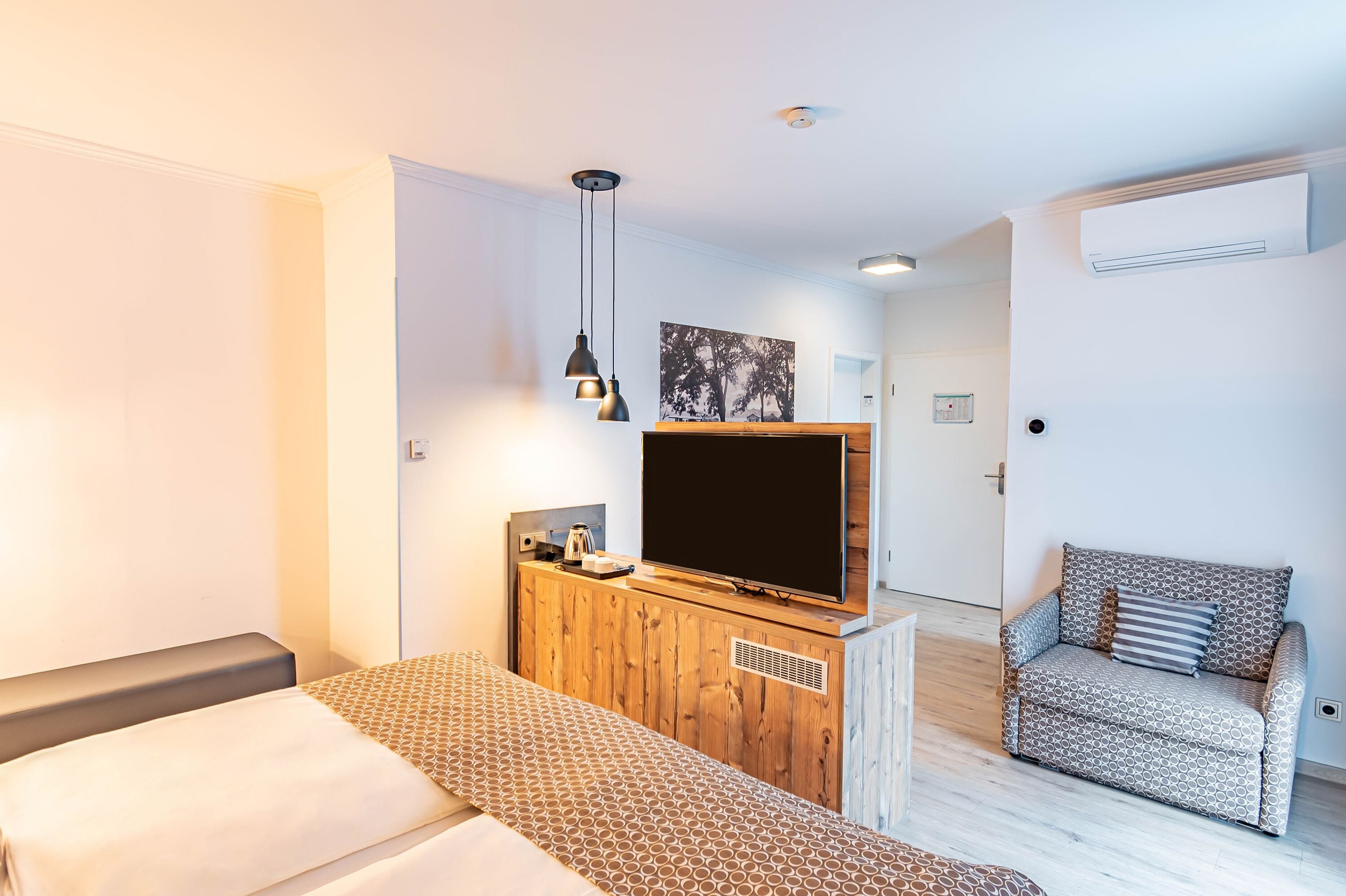 Ein modernes Hotelzimmer mit einem Bett, einem Fernseher auf einer Holzeinrichtung, einer gemusterten Couch und einem Bild an der Wand.