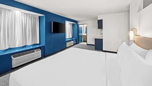 Ein Hotelzimmer mit einem großen Bett, einem Flachbildfernseher, einem Schreibtisch mit Lampe und einem durch eine offene Tür einsehbaren Badezimmer.