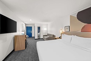 Ein Hotelzimmer mit Bett, Schreibtisch, Sessel, Sofa, Fernseher und einer Tür.