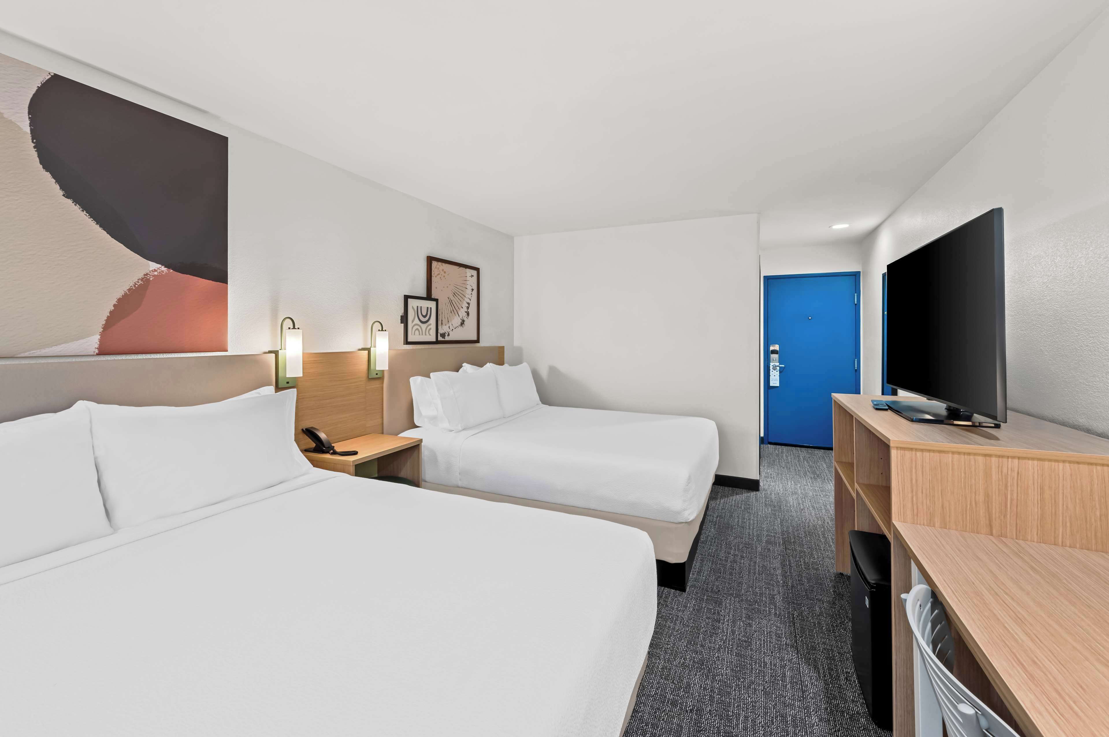 A hotel room with two beds, a desk, a TV, and a blue door.