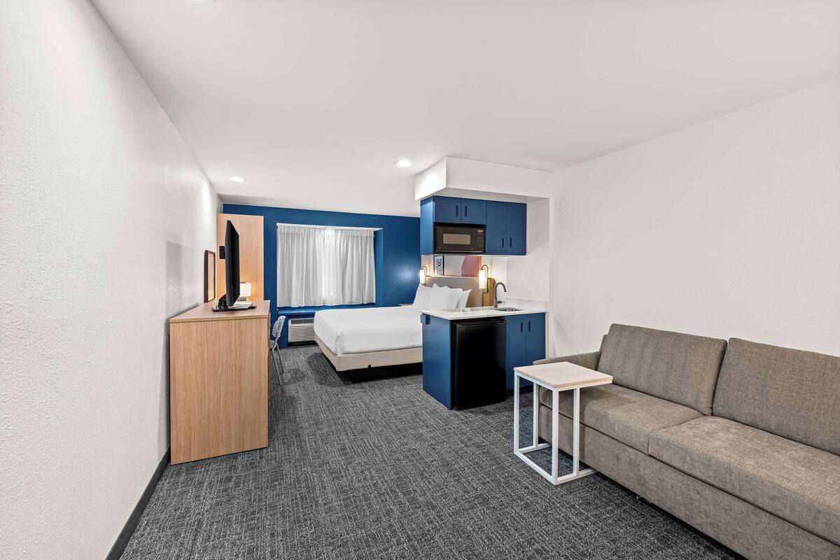 Ein Hotelzimmer mit Bett, einer Schlafcouch, einem kleinen Tisch, einem Schreibtisch, einer Mikrowelle und einem Waschbecken.