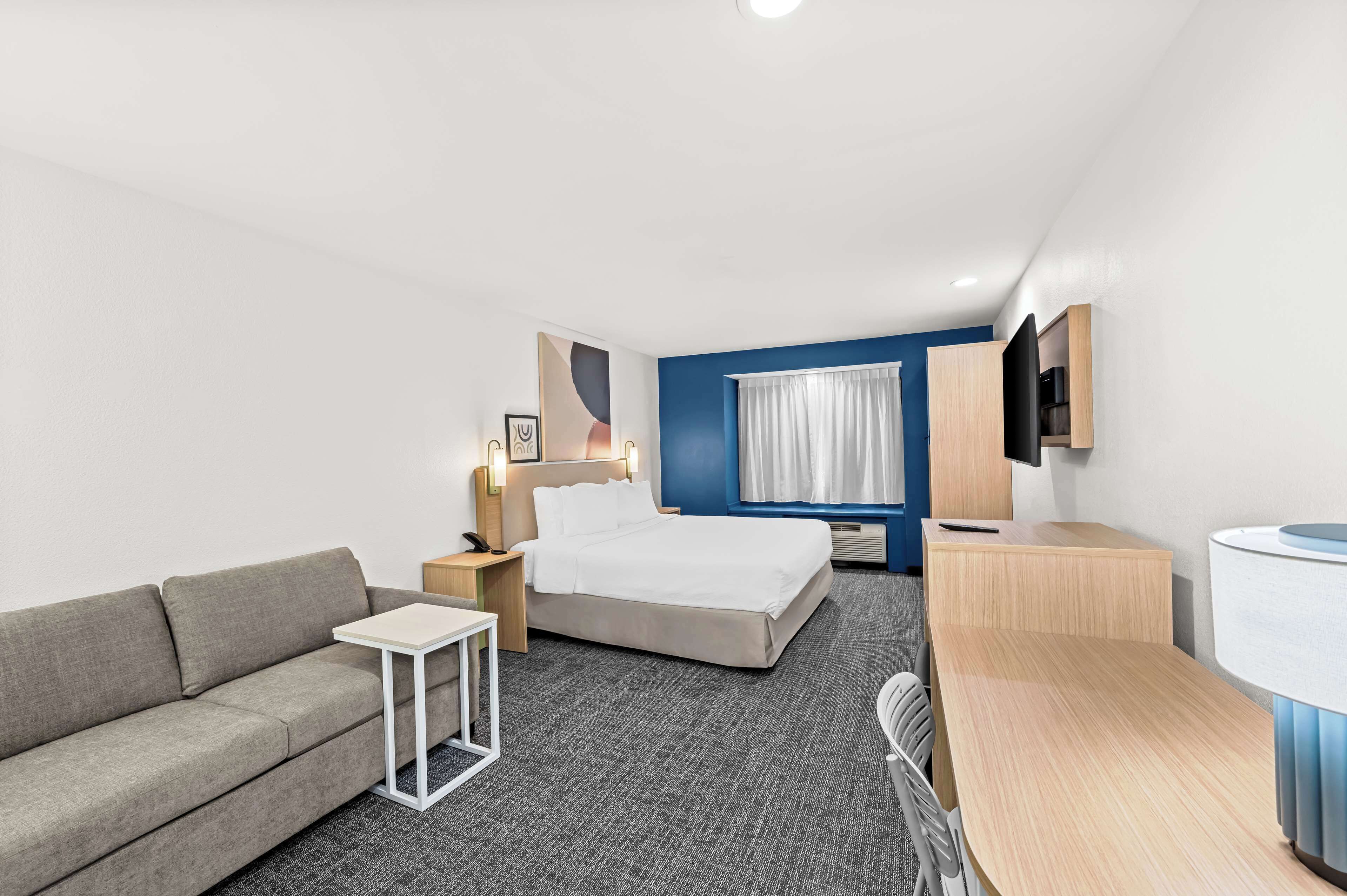 A hotel room with a bed, a sofa, a small table, a desk, and a TV.