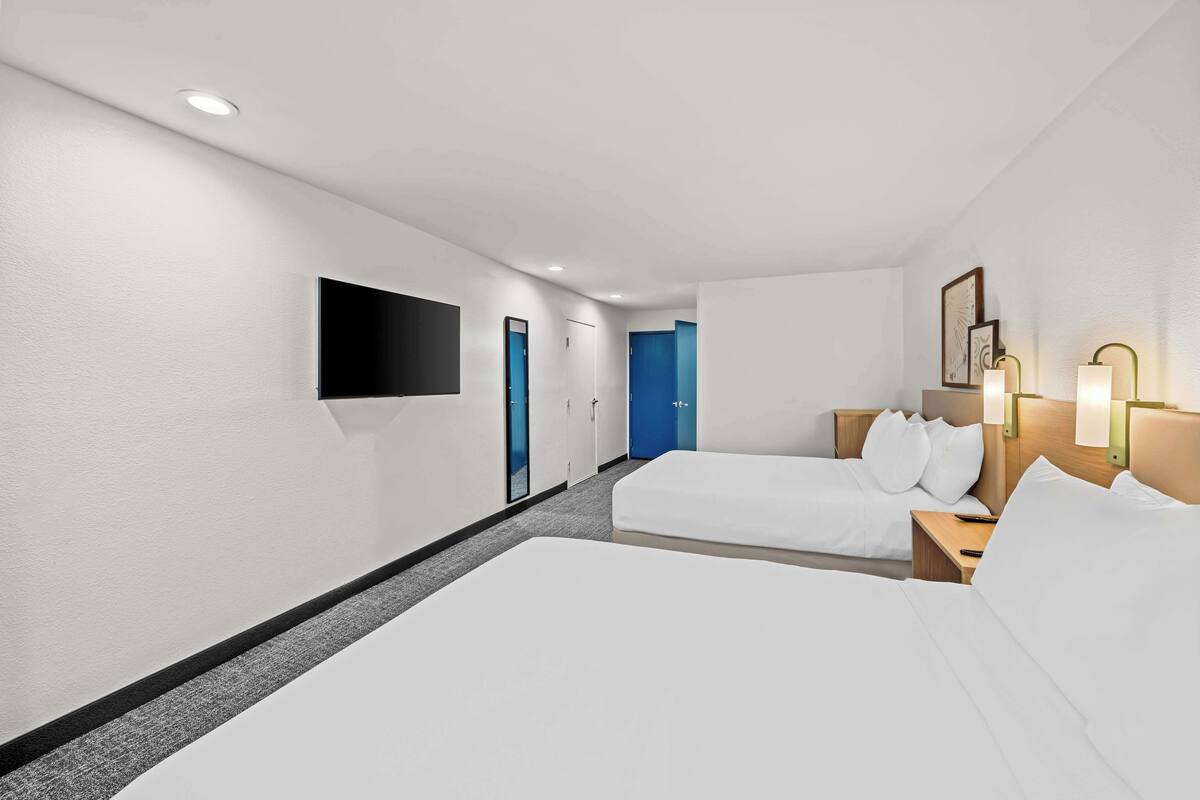 Ein Hotelzimmer mit zwei Betten, einem wandmontierten Flachbildfernseher und einer blauen Tür.