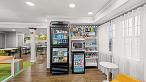 Eine moderne Hotelhalle mit Sitzgelegenheit, einem Automaten und einer kleinen Verkaufstheke.