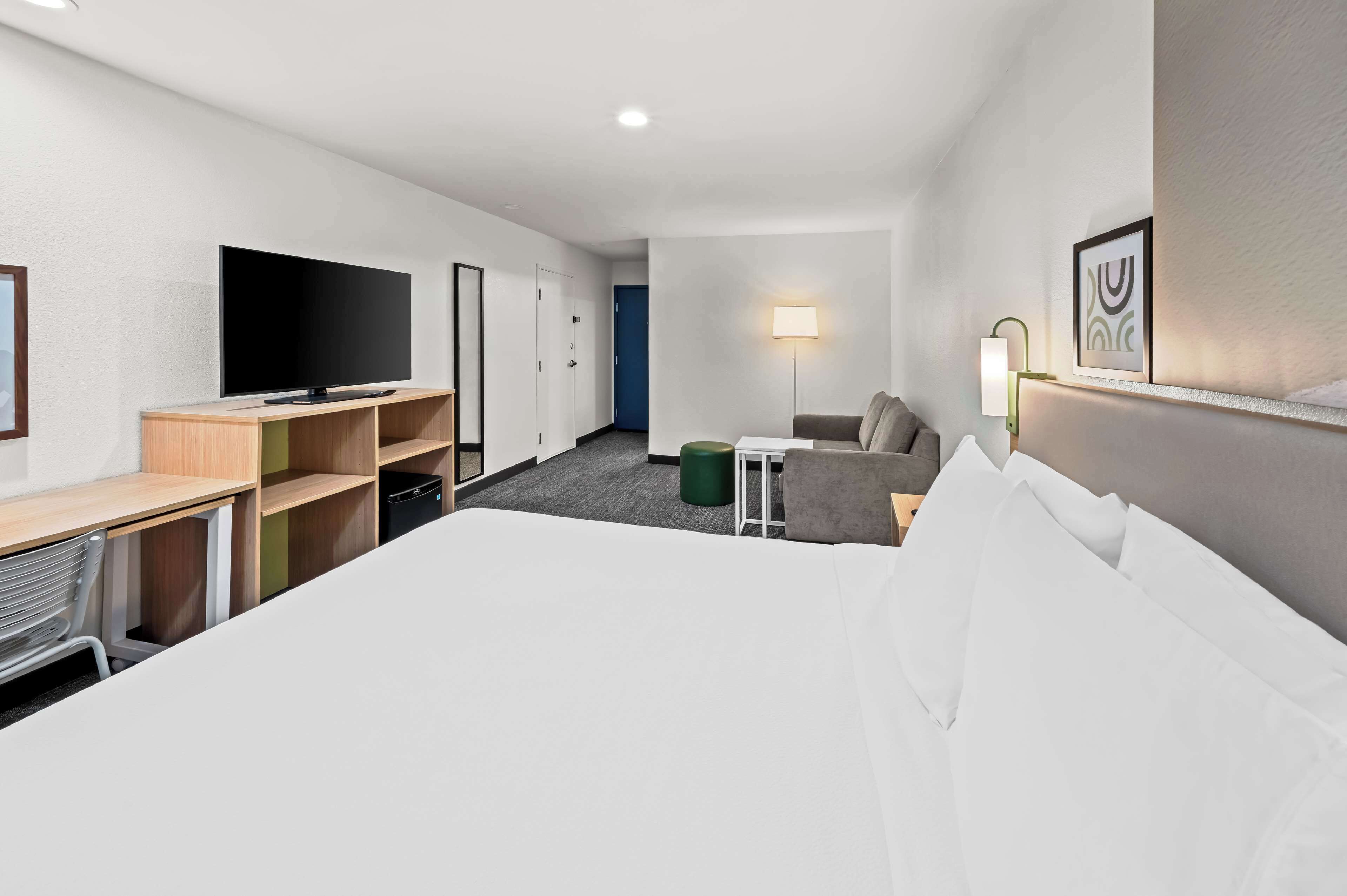 A hotel room with a large bed, a desk with a computer, a television, a lamp, and a small seating area.