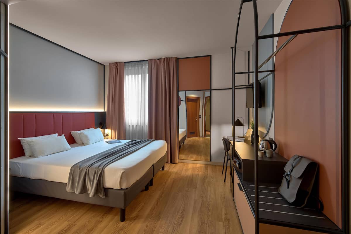 A modern hotel room with a bed, bedside table, mirror, and a view of the hallway.