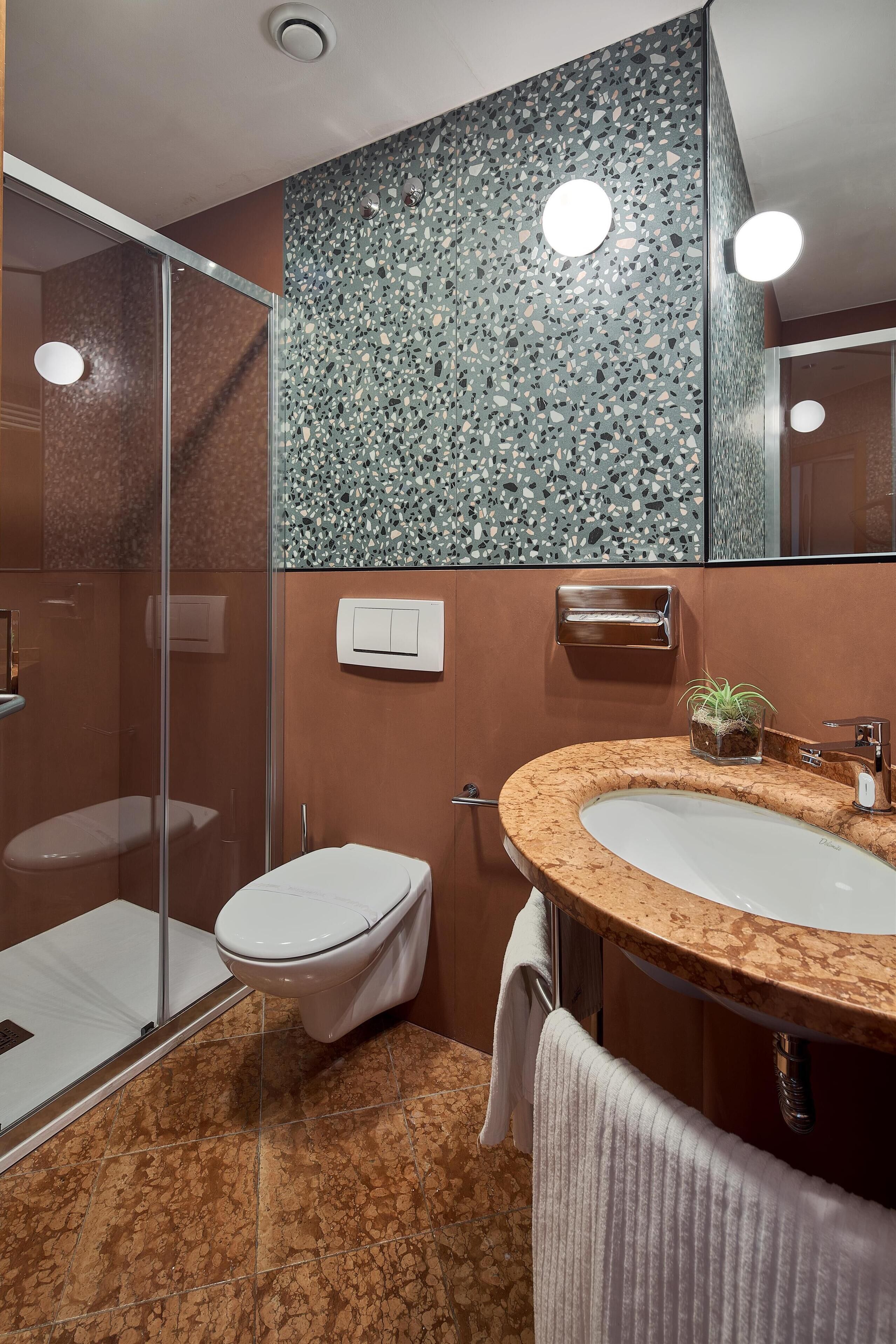 A bathroom with a glass shower enclosure, a toilet, a sink with a marble countertop, and a mirror.