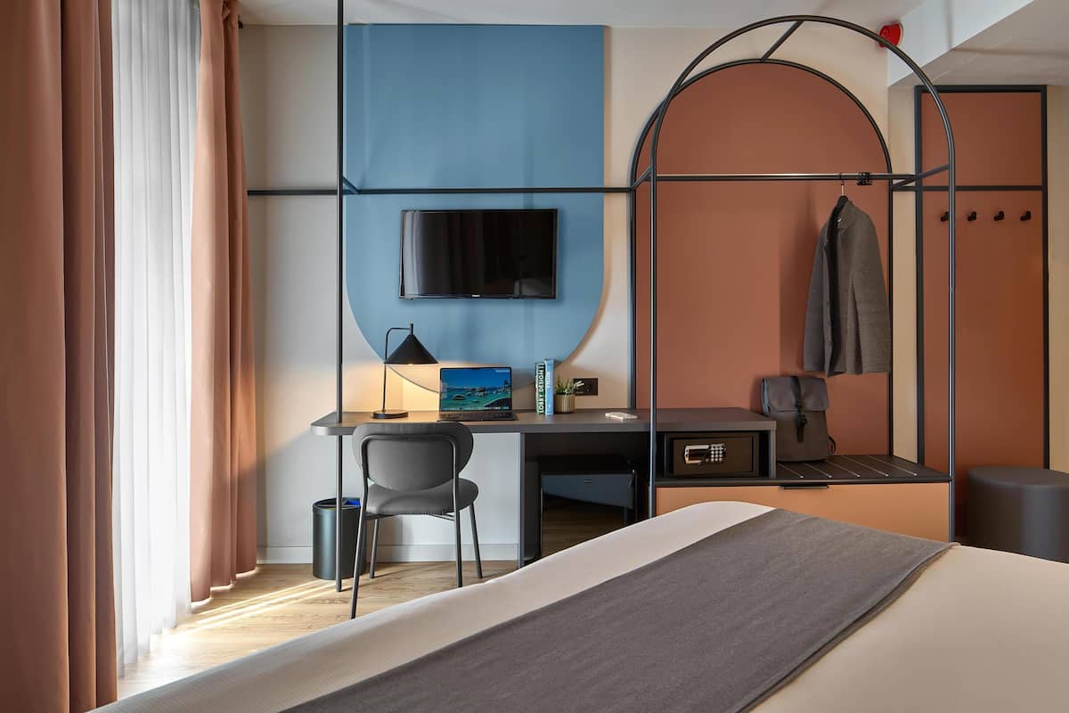 A hotel room with a bed, desk, chair, TV, and a wardrobe.