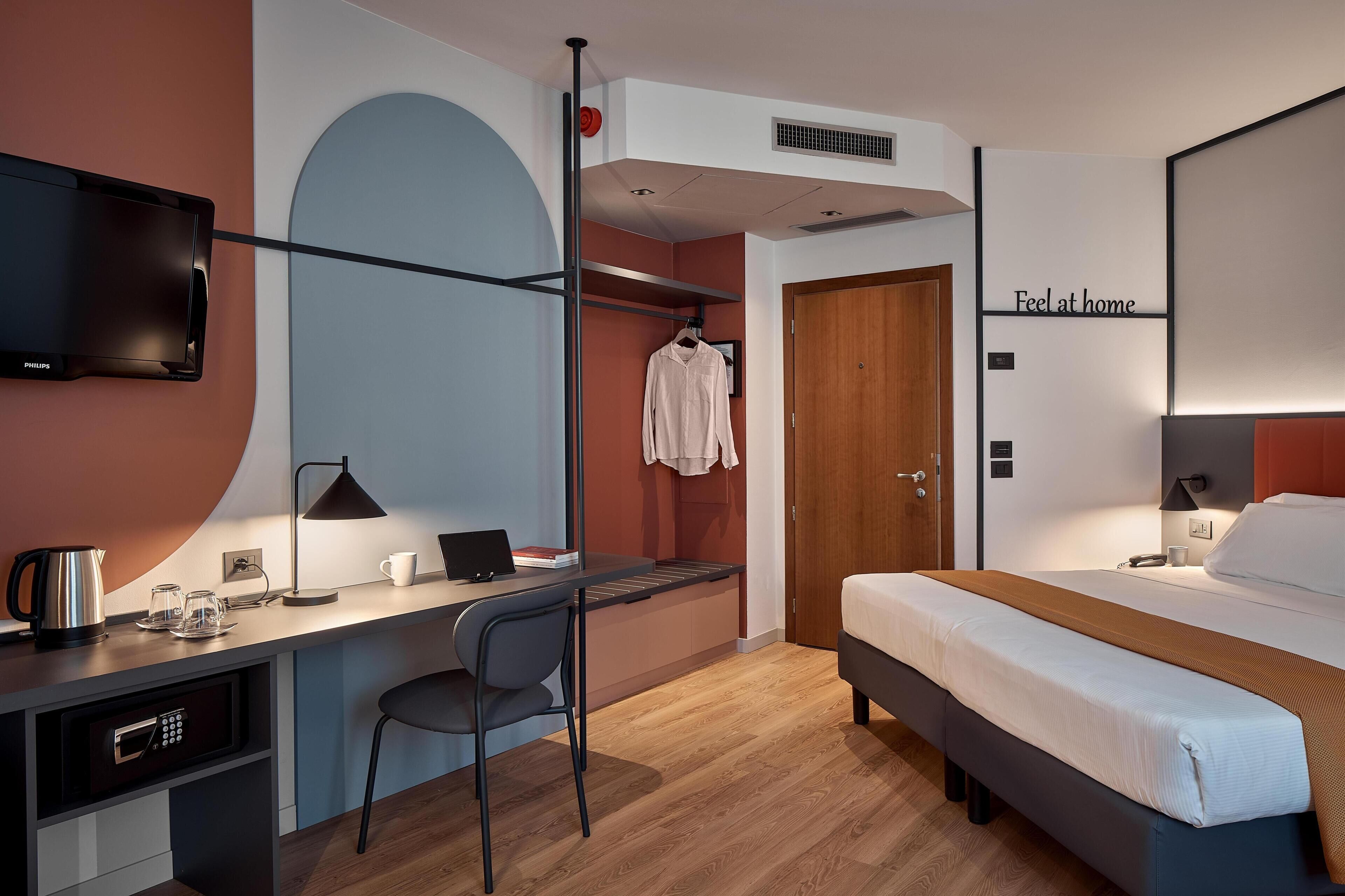 A hotel room with a bed, desk, chair, TV, and a wardrobe.