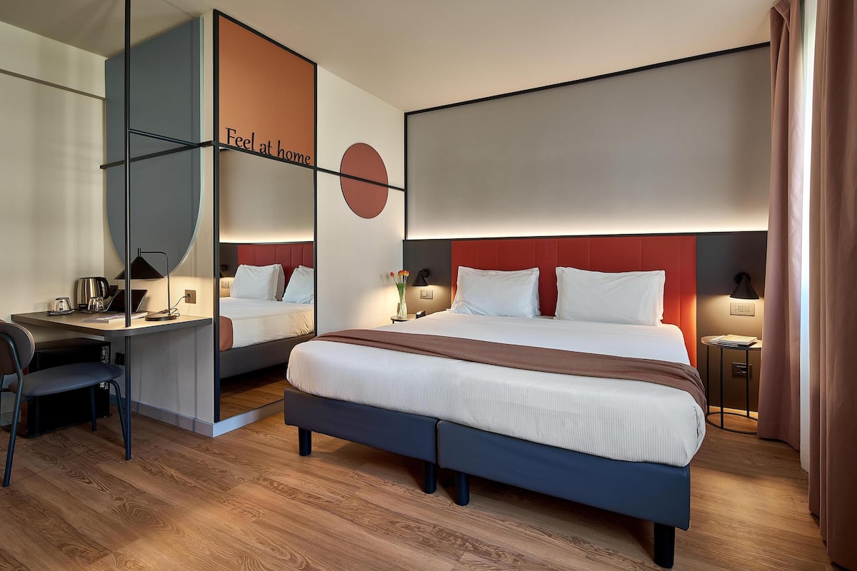 A modern hotel room with a large bed, a desk, and a mirror.