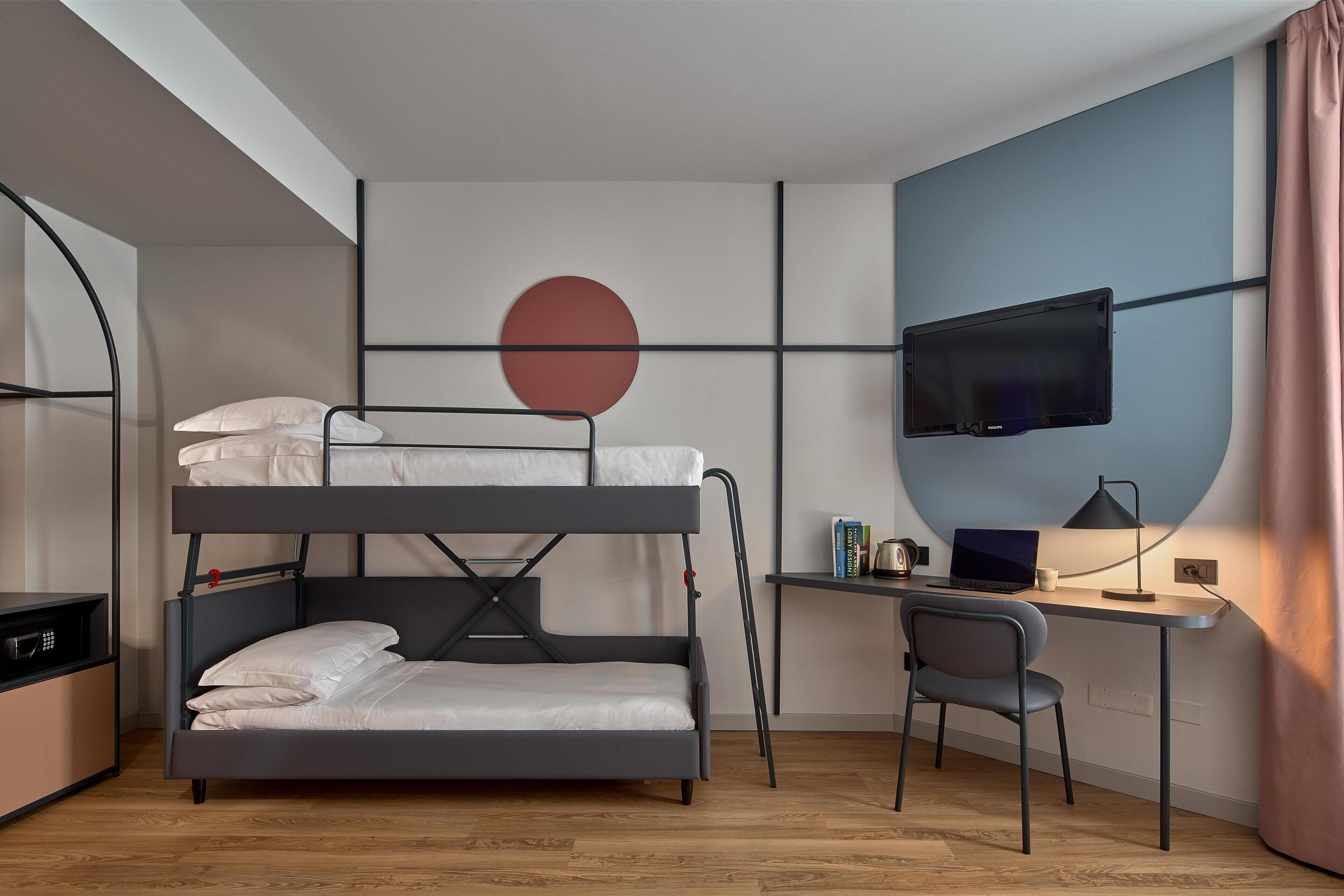 A bunk bed with a desk and chair, a television, and a wall-mounted circular decoration.