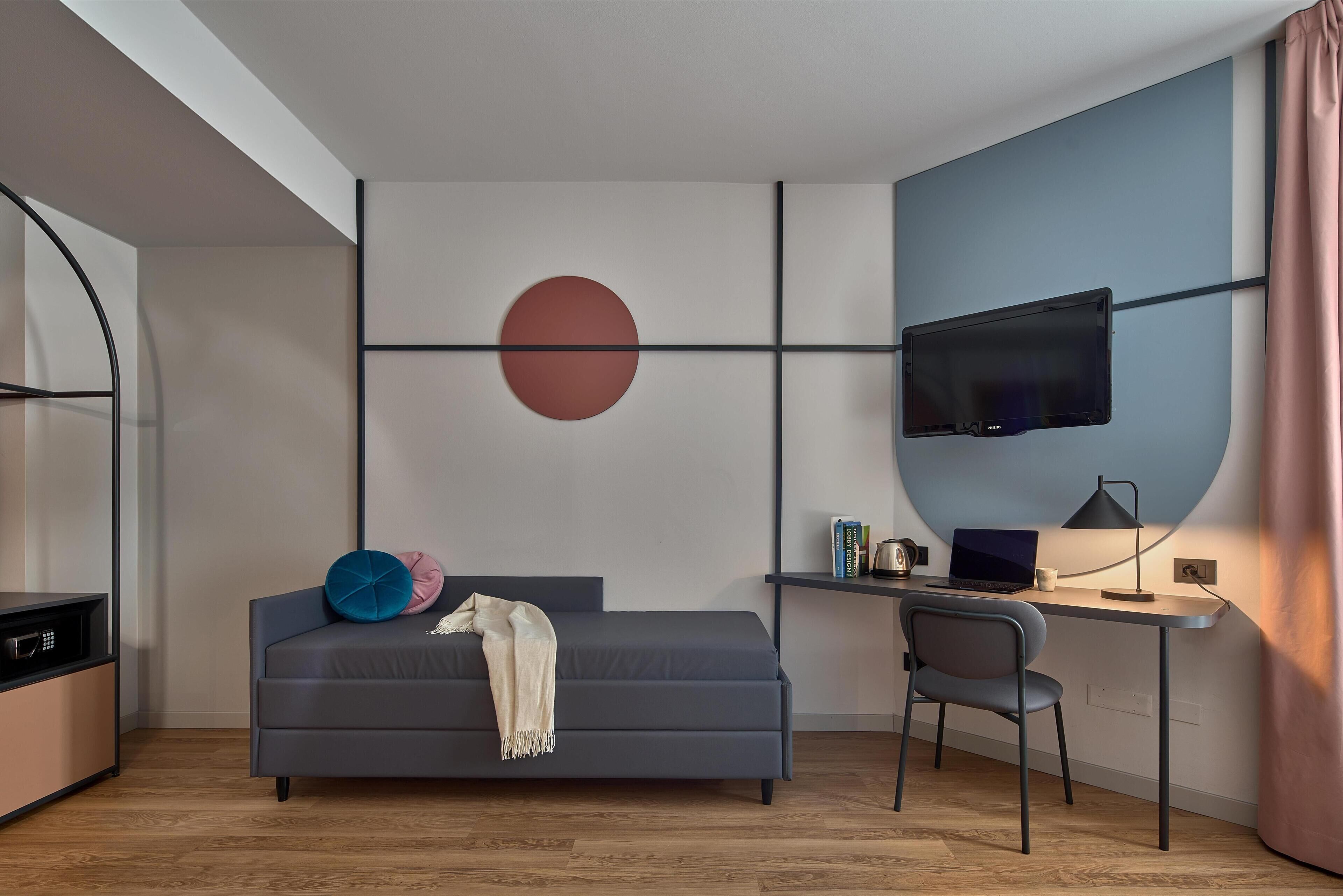 A modern room with a bed, a desk, a chair, a TV, and a large circular wall decoration.