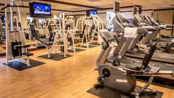 A gym with cardio machines, weight machines, and a television displaying news.