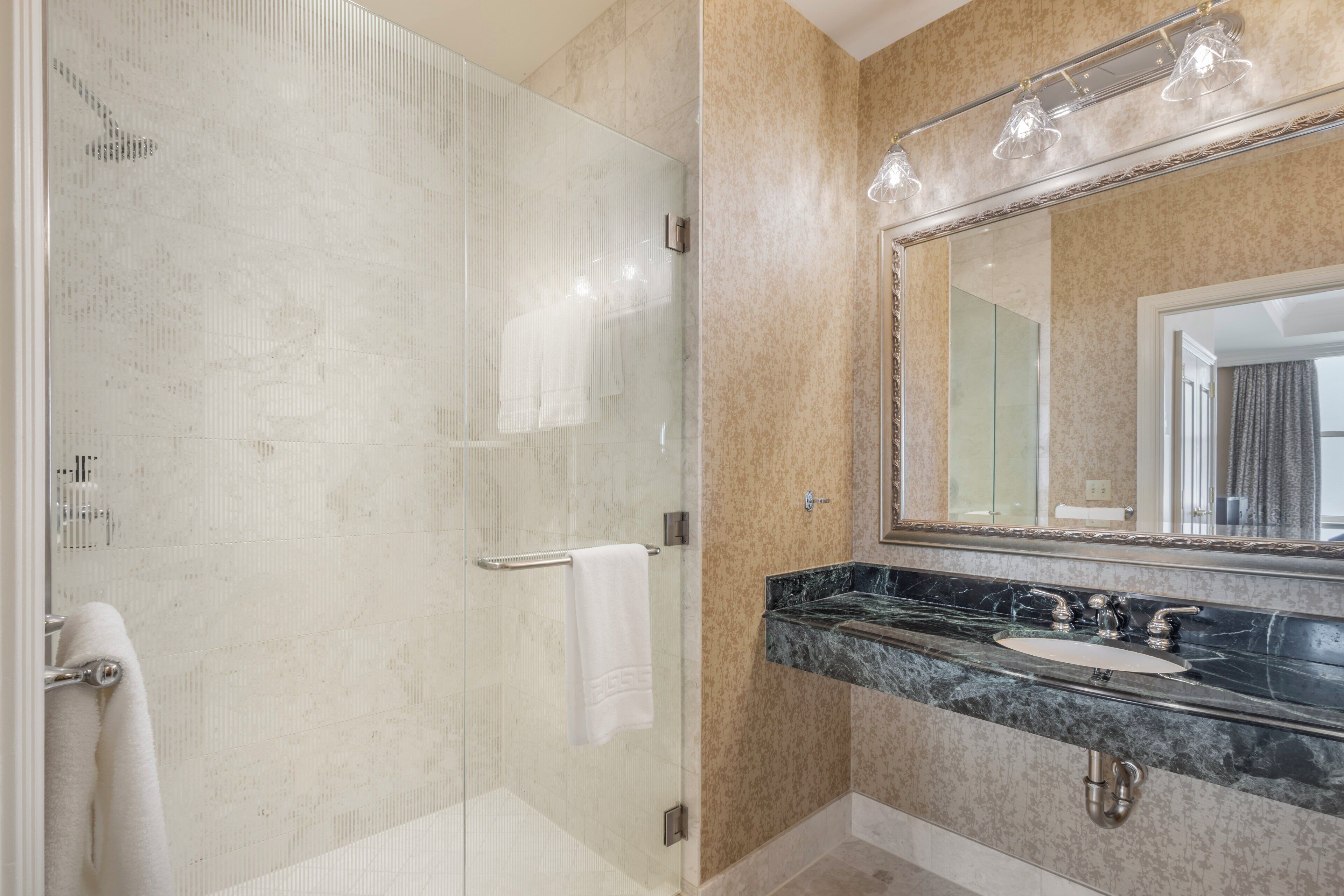 A modern bathroom with a glass-enclosed shower, a marble sink, and a large mirror with lights.