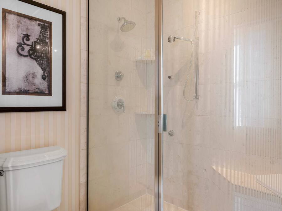 A bathroom with a glass-enclosed shower, a toilet, and a framed artwork on the wall.