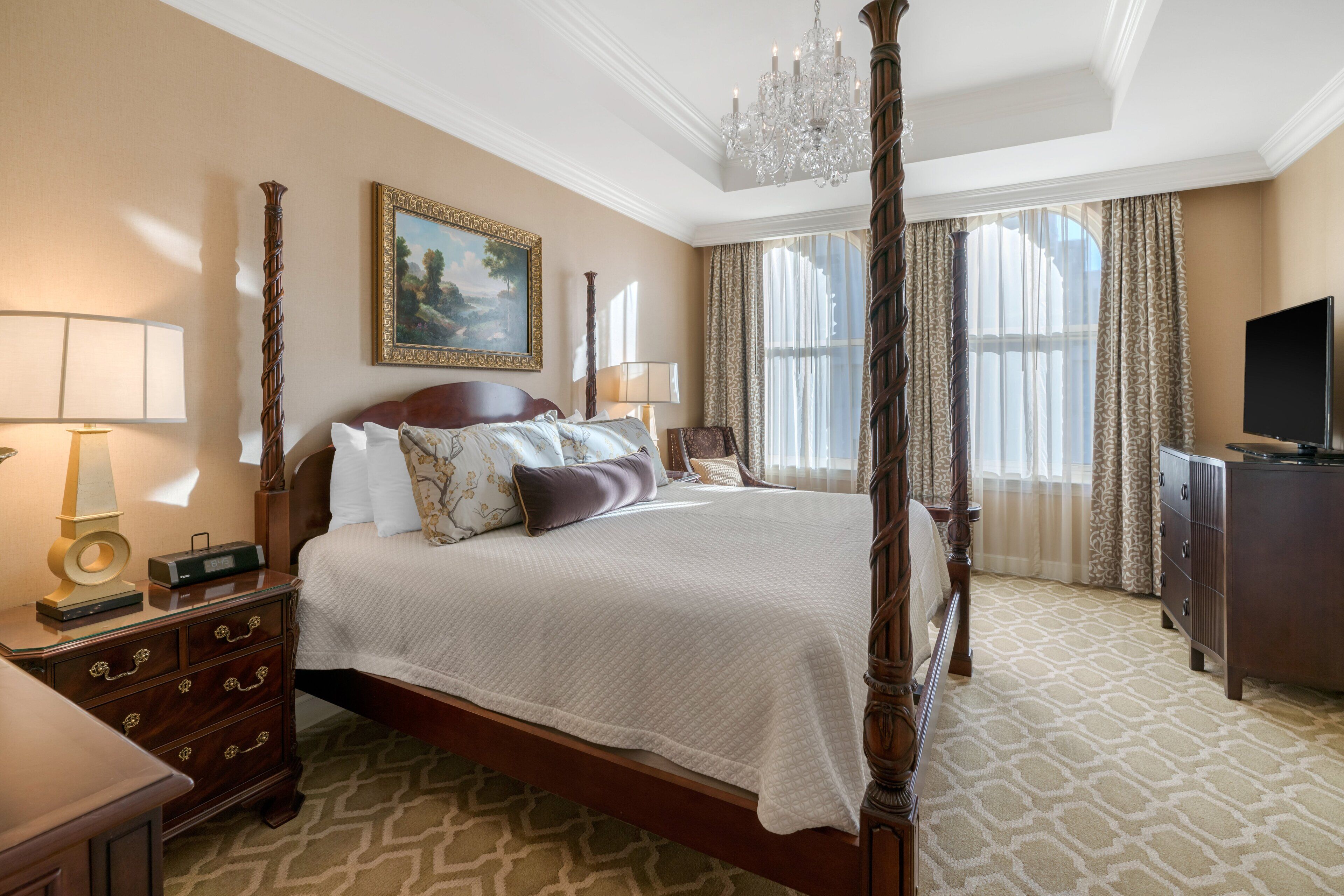 A four-poster bed with a chandelier, a television, and a dresser in a hotel room.