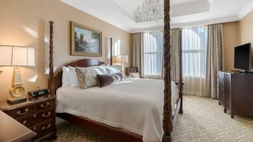 A four-poster bed with a chandelier, a television, and a dresser in a hotel room.