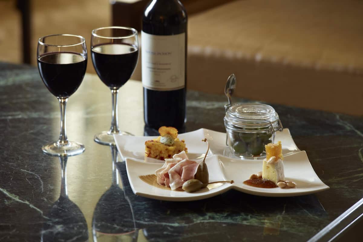 A table with two wine glasses, a bottle of wine, and a plate with food and a jar.