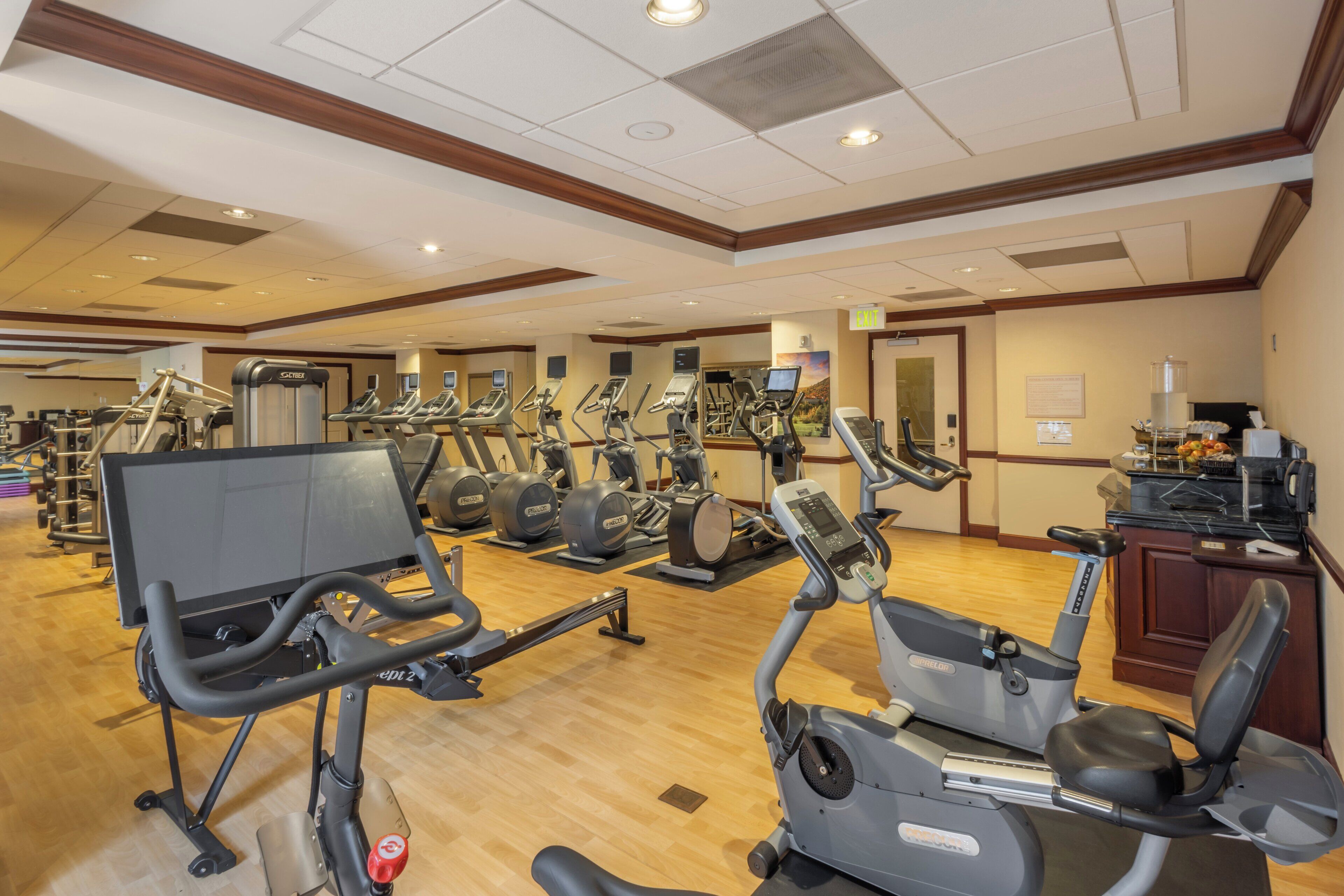 A gym with various exercise machines, including treadmills and stationary bikes, and a reception desk in the background.
