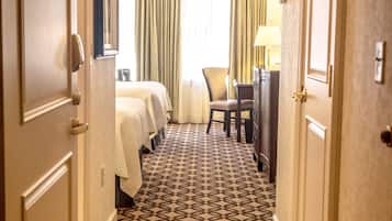 A hotel hallway with patterned carpet, a bed, a desk, and a chair.