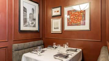 A dining area with a table set for two, framed pictures on the wall, and a bench.