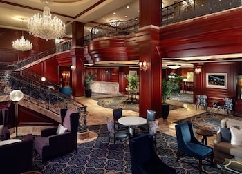 A spacious living room with a large sofa, armchairs, a coffee table, and a dining area with a chandelier. at Omni San Francisco Hotel