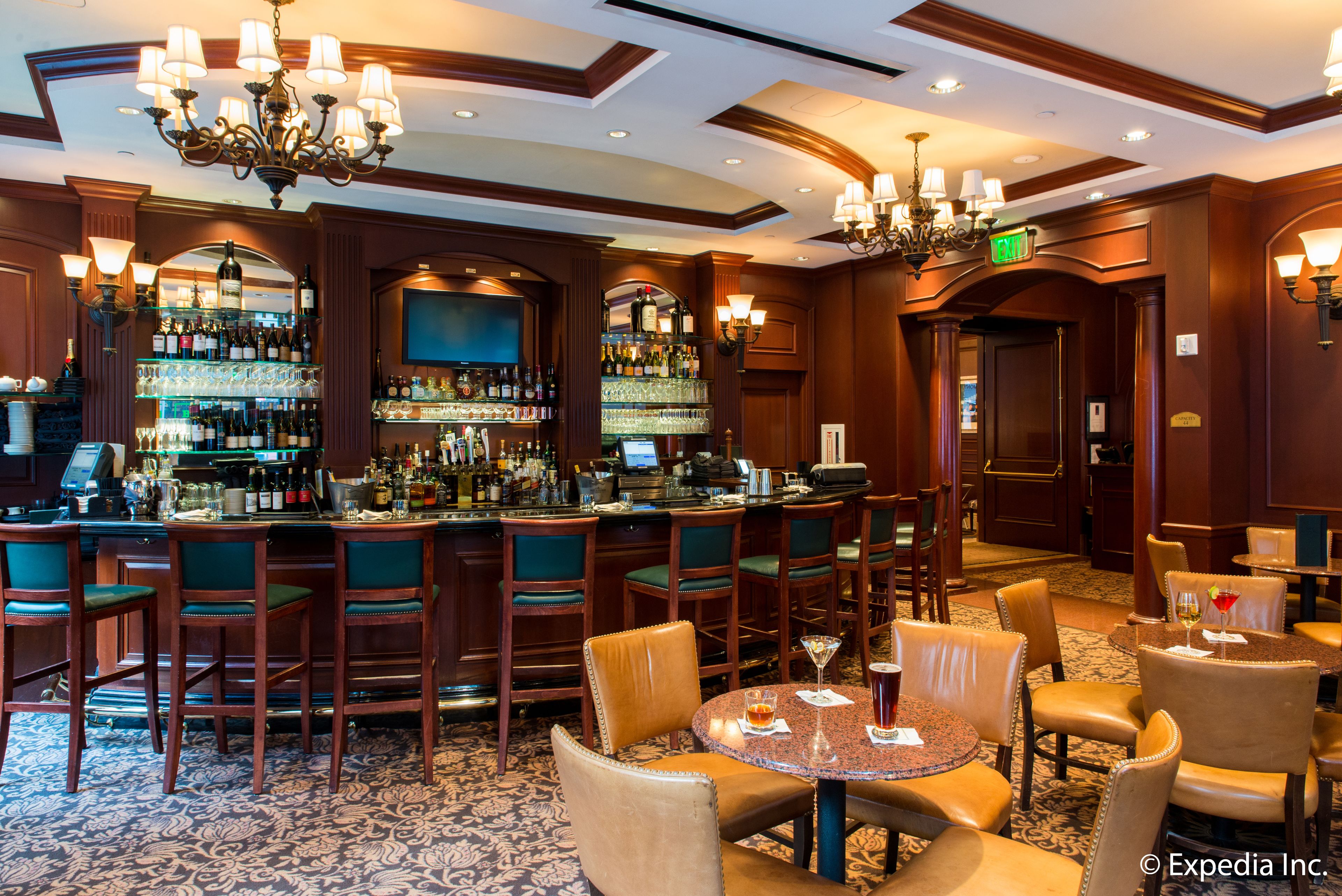 A bar area with multiple seating options, a well-stocked bar, and a chandelier.