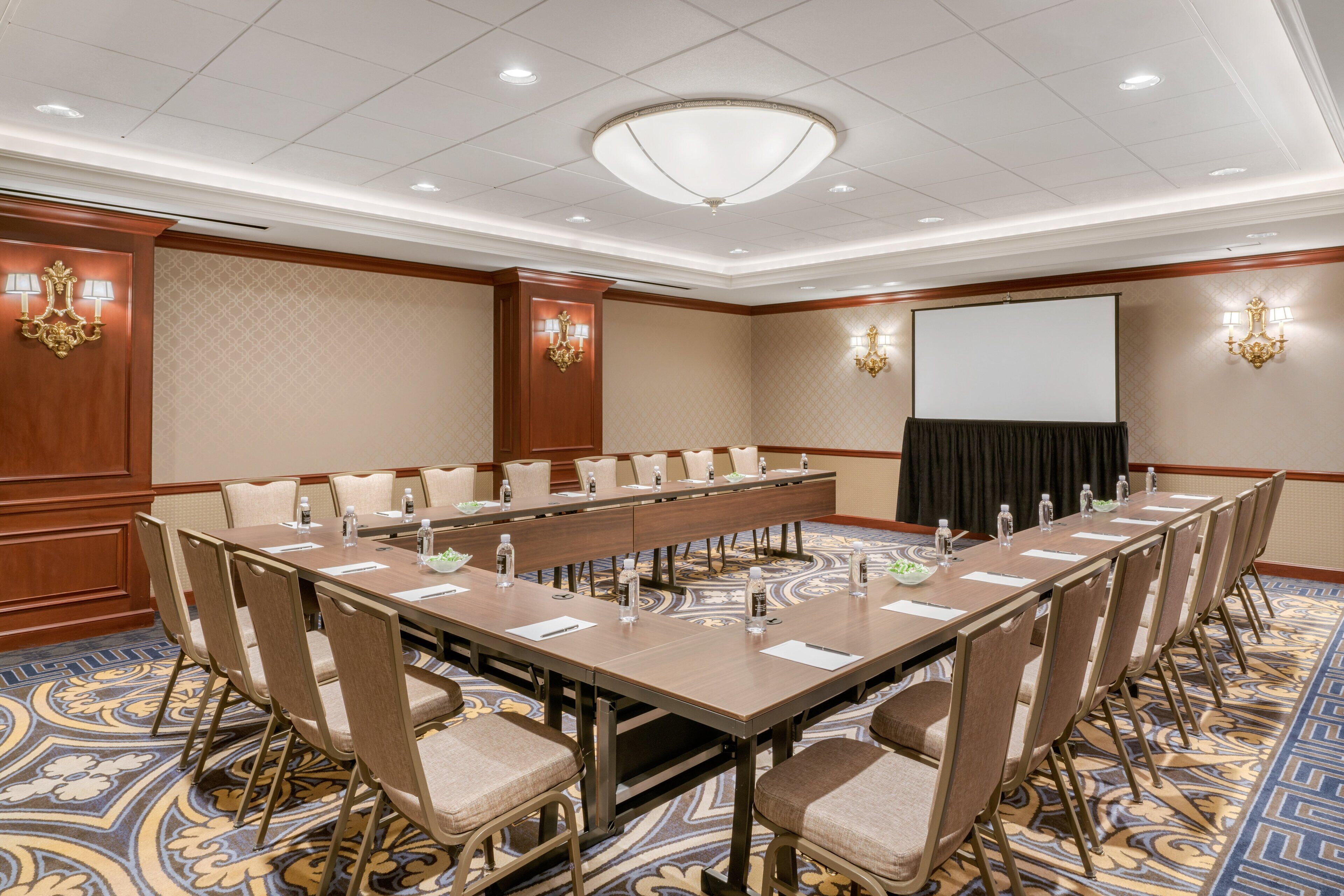 A conference room with a long table, chairs, a projector screen, and a carpeted floor.