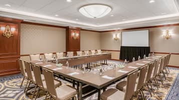 A conference room with a long table, chairs, a projector screen, and a carpeted floor.