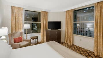A hotel room with a large bed, a television, a chair, a small table, and a dresser.