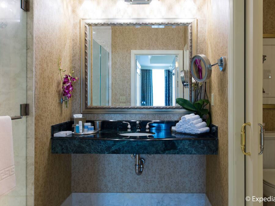 A bathroom with a marble sink, a large mirror, and a toilet visible through an open door.