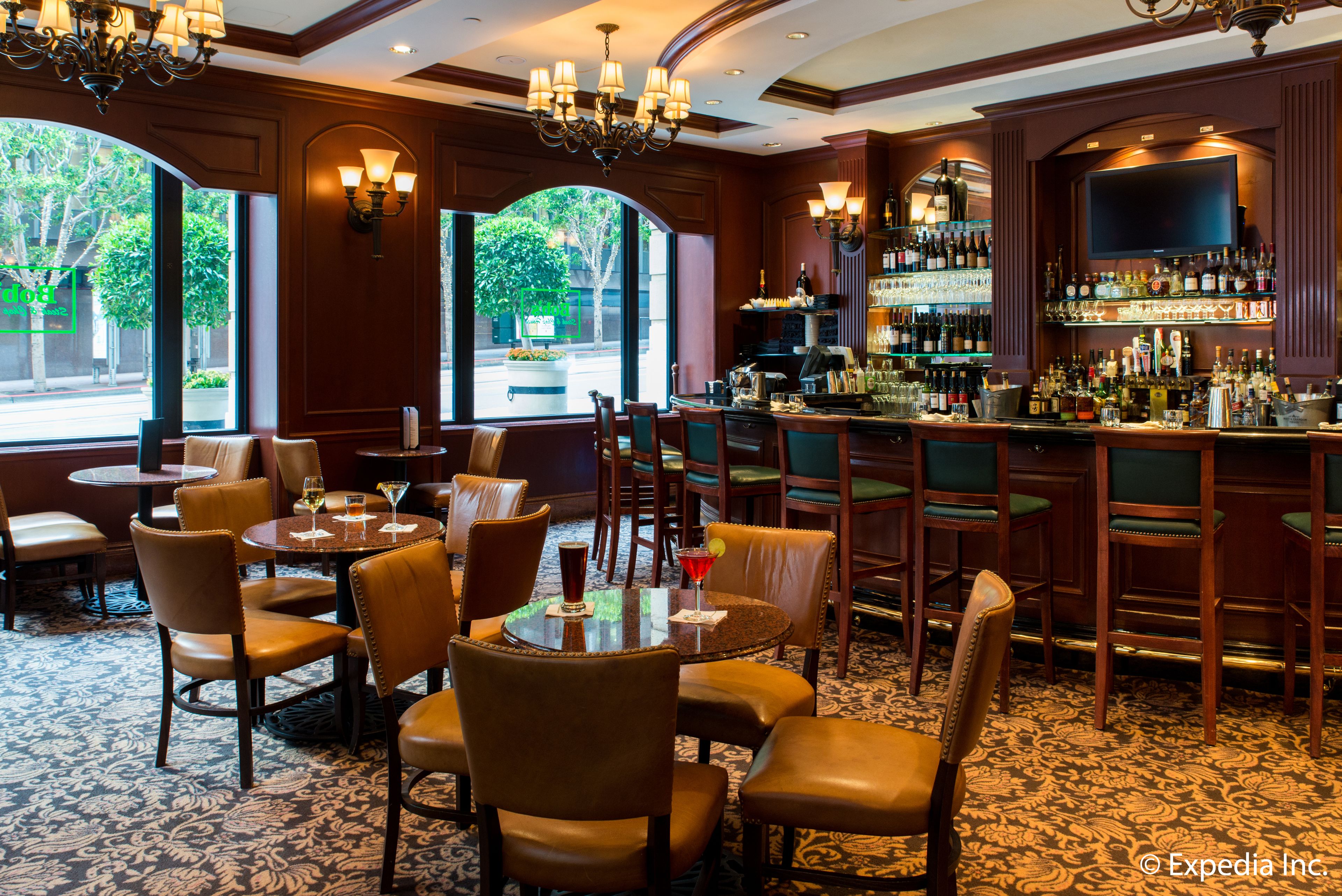 Een bar met verschillende zitmogelijkheden, zoals ronde tafels en barstoelen, en een goed gevulde bar met diverse flessen en glazen.