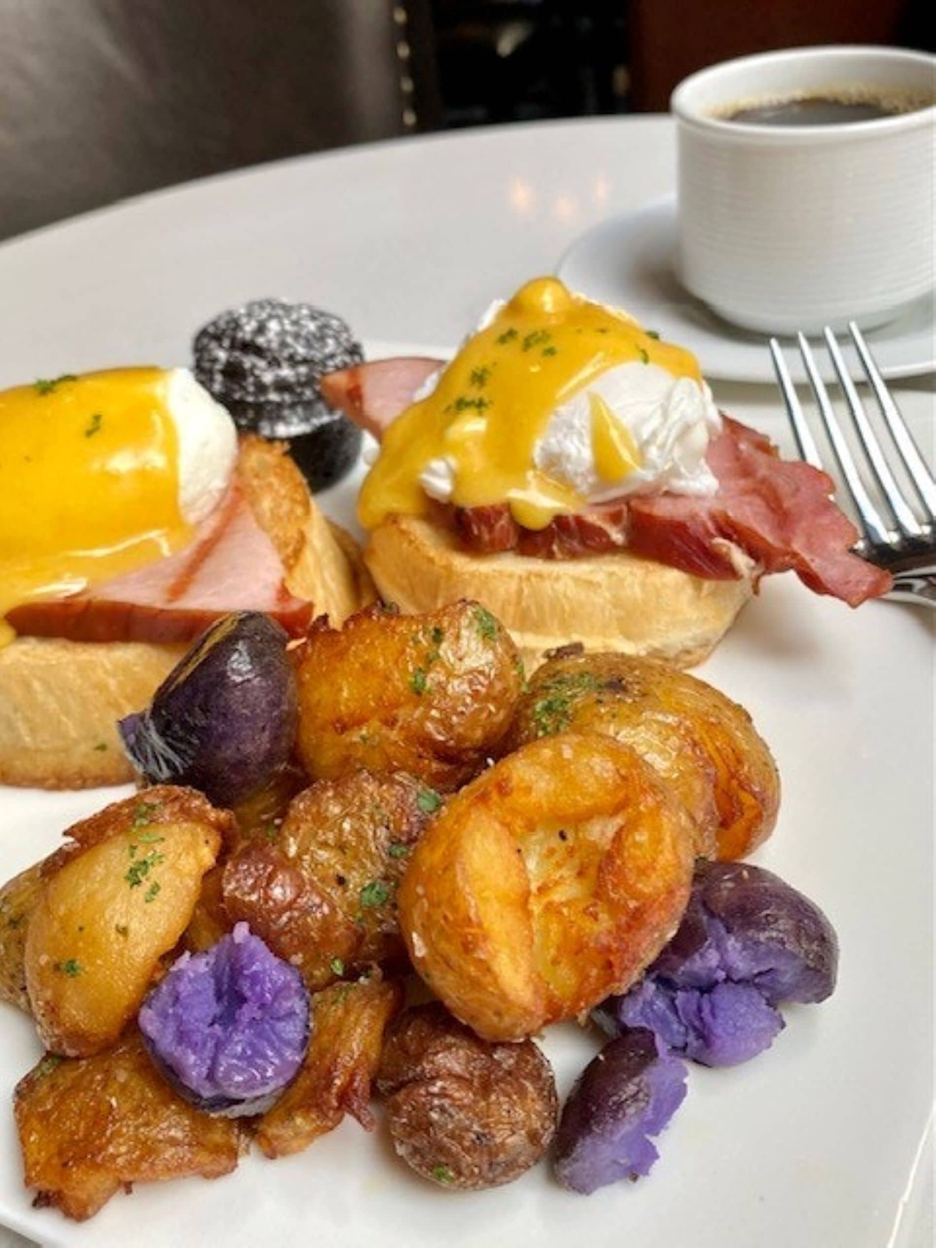 A plate of food with eggs benedict, ham, and roasted potatoes.