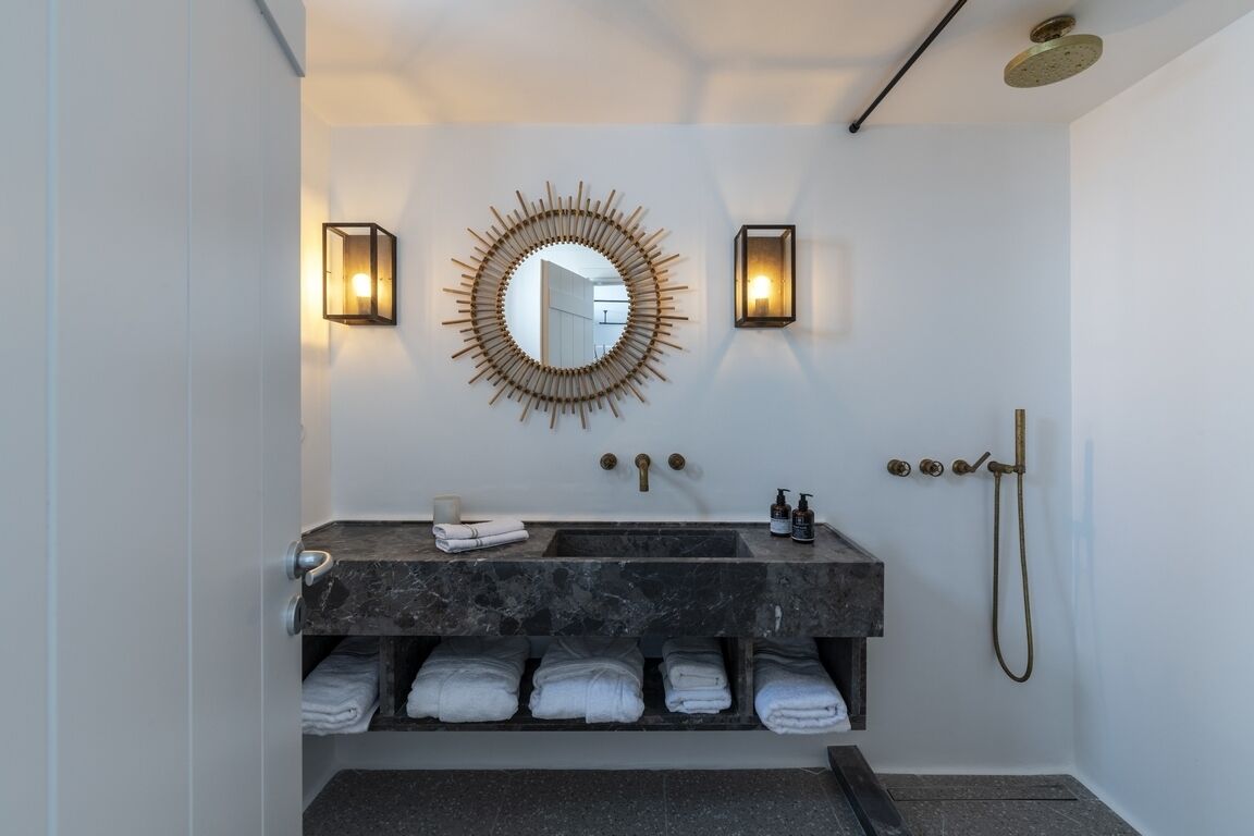 A modern bathroom with a marble sink, a sunburst mirror, wall-mounted lights, a shower, and neatly folded towels.