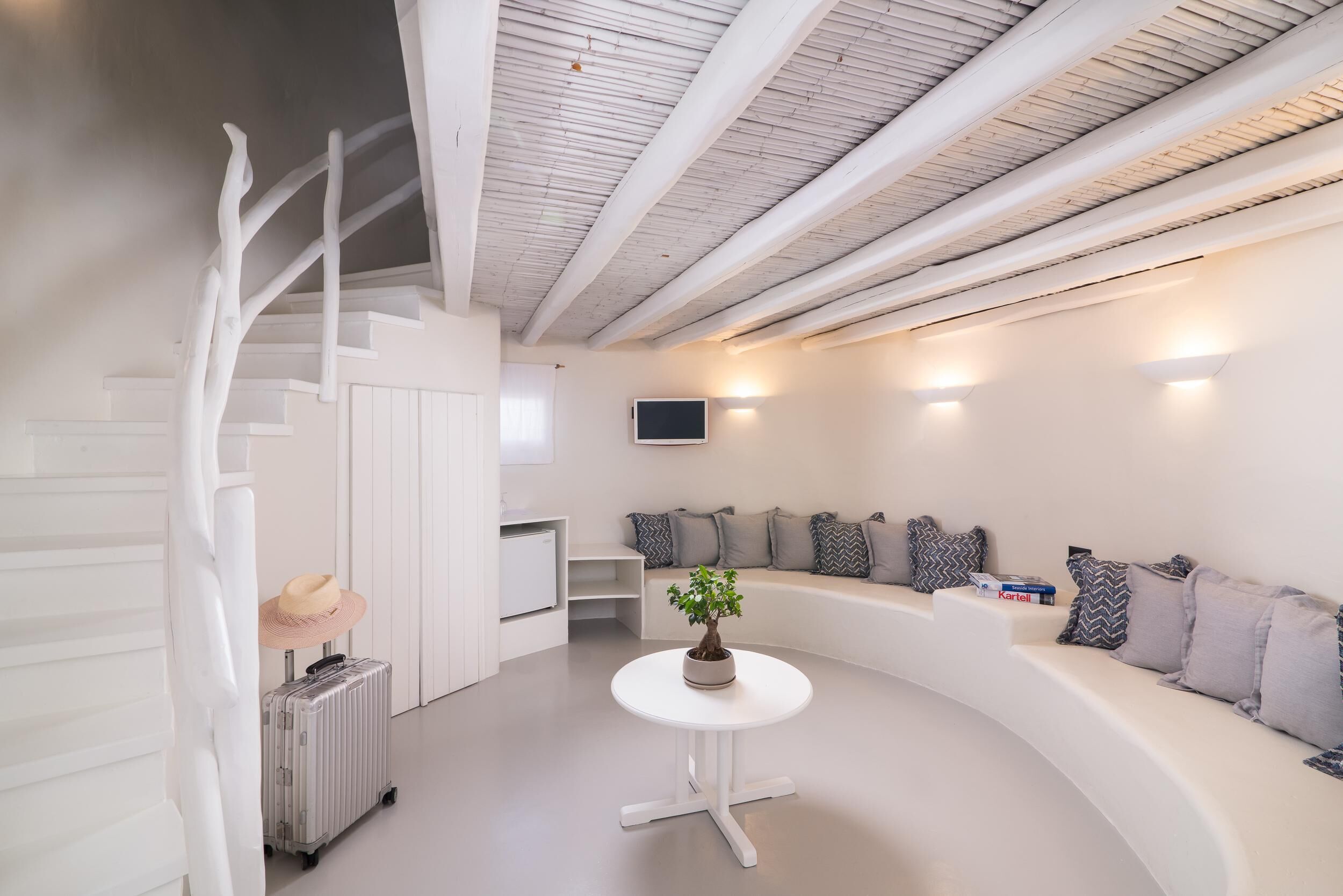 Ein modernes Interieur mit Treppe, einem runden Tisch mit Pflanze, einer Couch mit Kissen und einem an der Wand befestigten Flachbildfernseher.
