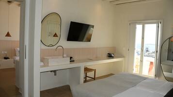 A modern hotel room with a large bed, a bathroom with a sink and mirror, and a TV mounted on the wall.