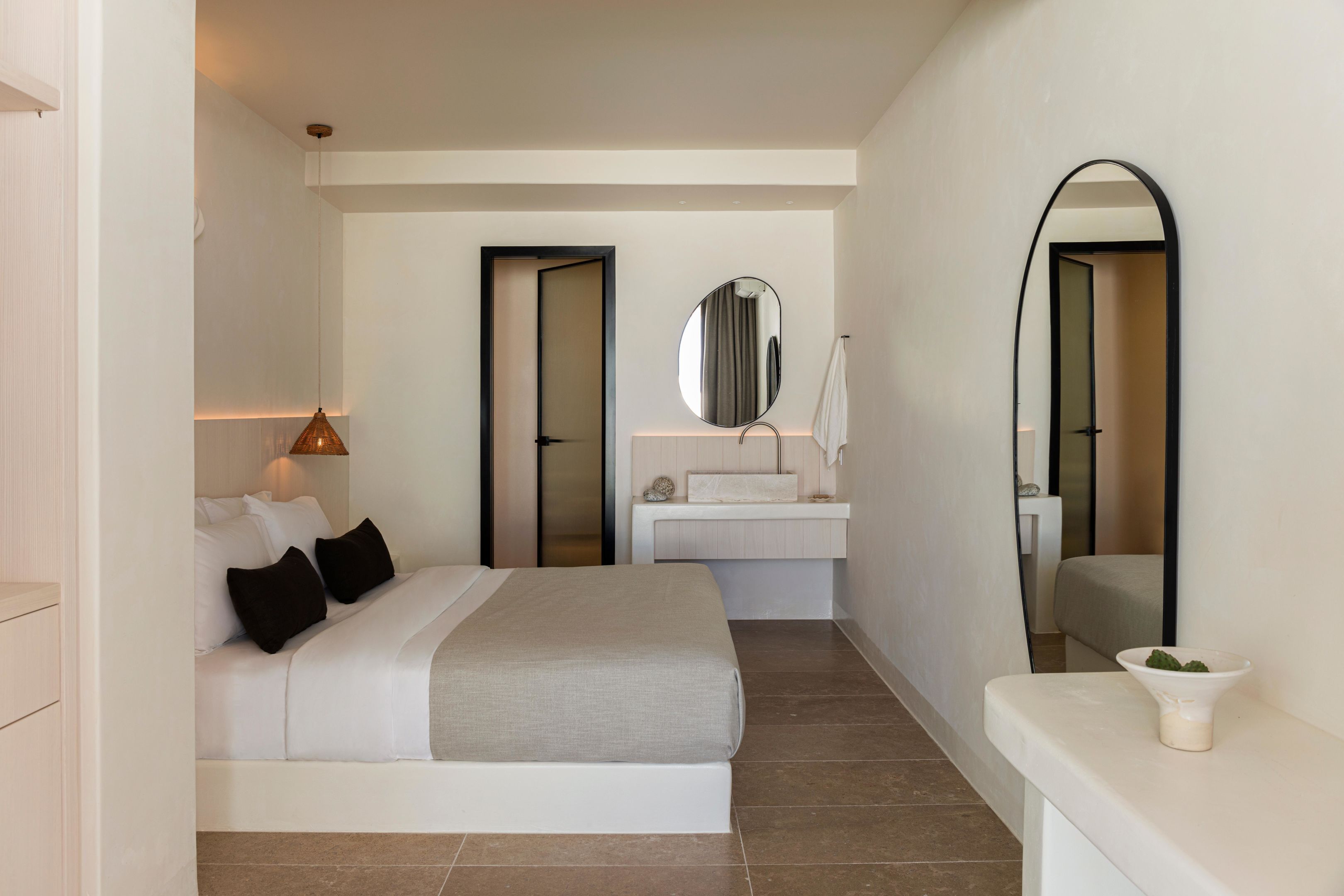 A modern bedroom with a bed, bedside table, and a bathroom with a sink and mirror.