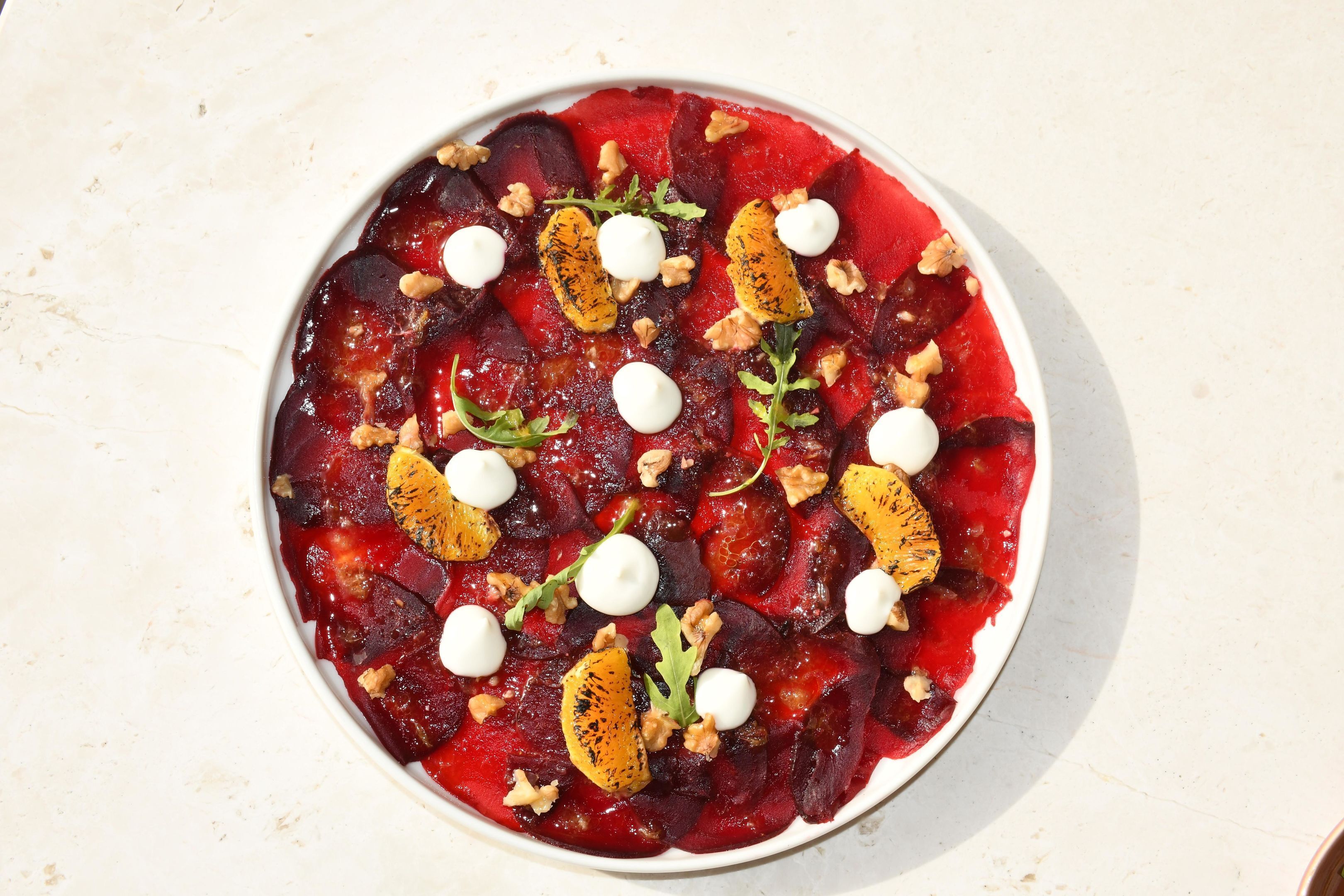 Une assiette ronde blanche, sur laquelle est servie une salade de betteraves, garnie de noix, de tranches d’orange et de quenelles de crème.