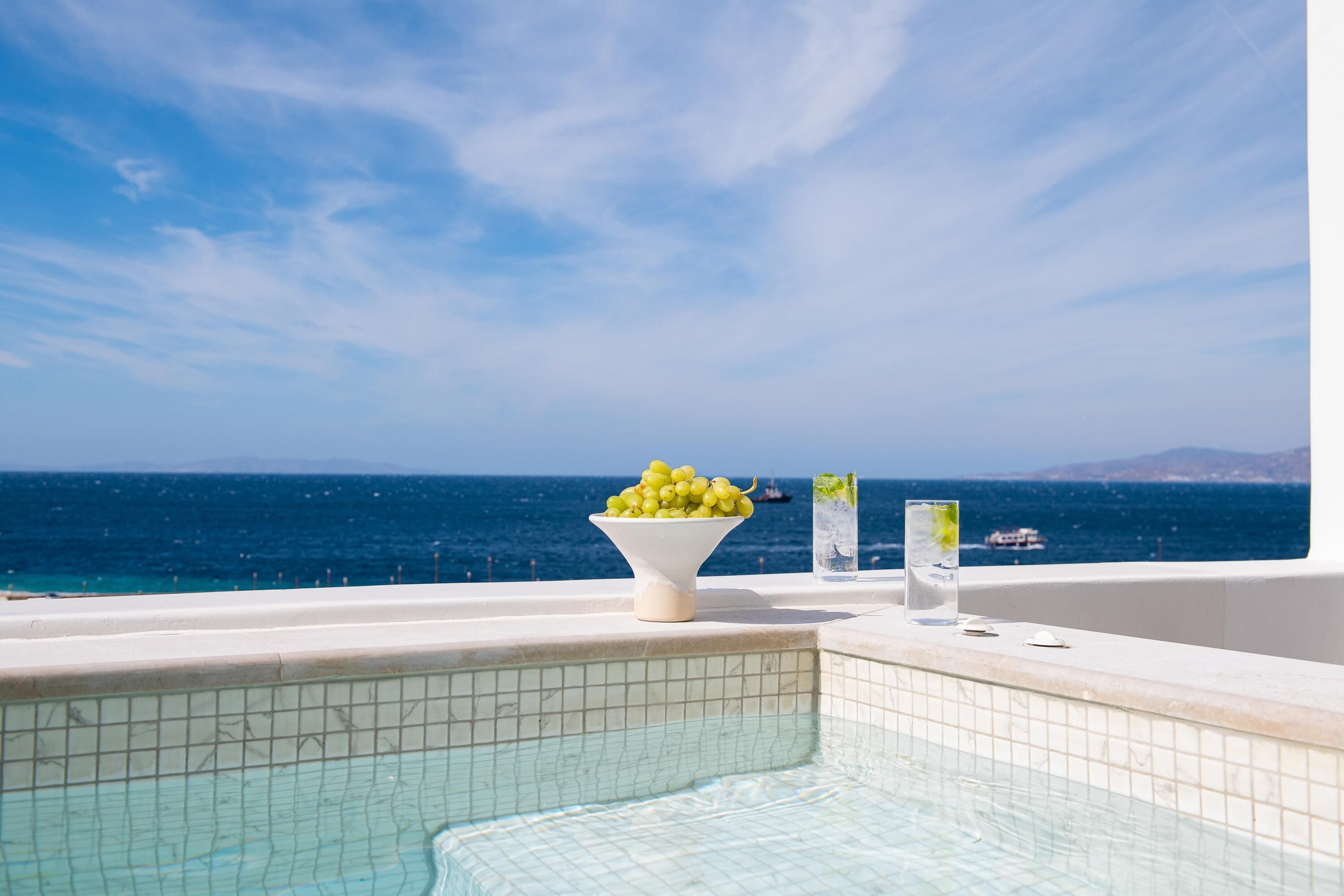 Une vue sur la piscine, avec un ciel bleu dégagé, un bol de raisins et un verre d’eau.