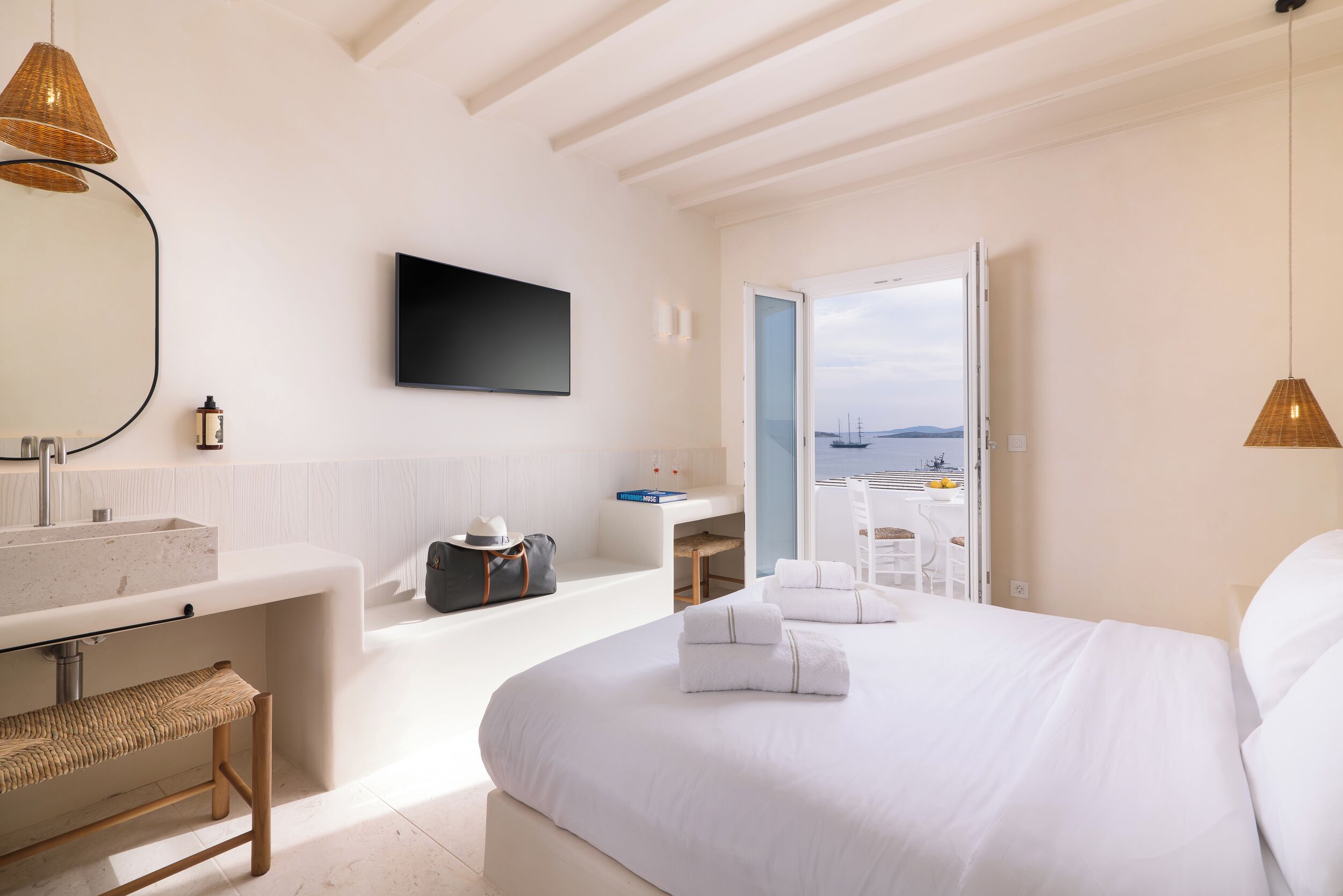 A modern hotel room with a large bed, a bathroom with a bathtub, a desk, and a view of the sea.
