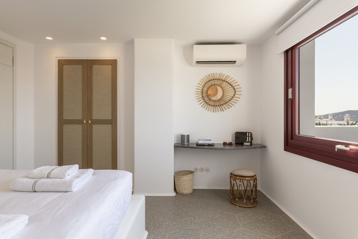 A modern hotel room with a bed, a small seating area, an air conditioning unit, and a view of the city.