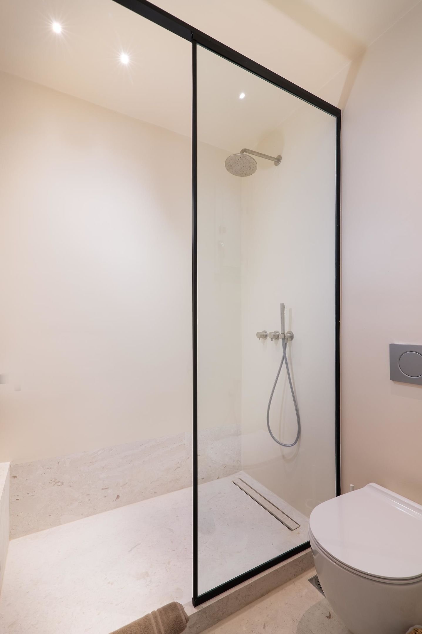 A modern bathroom with a glass-enclosed shower, a toilet, and a marble floor.