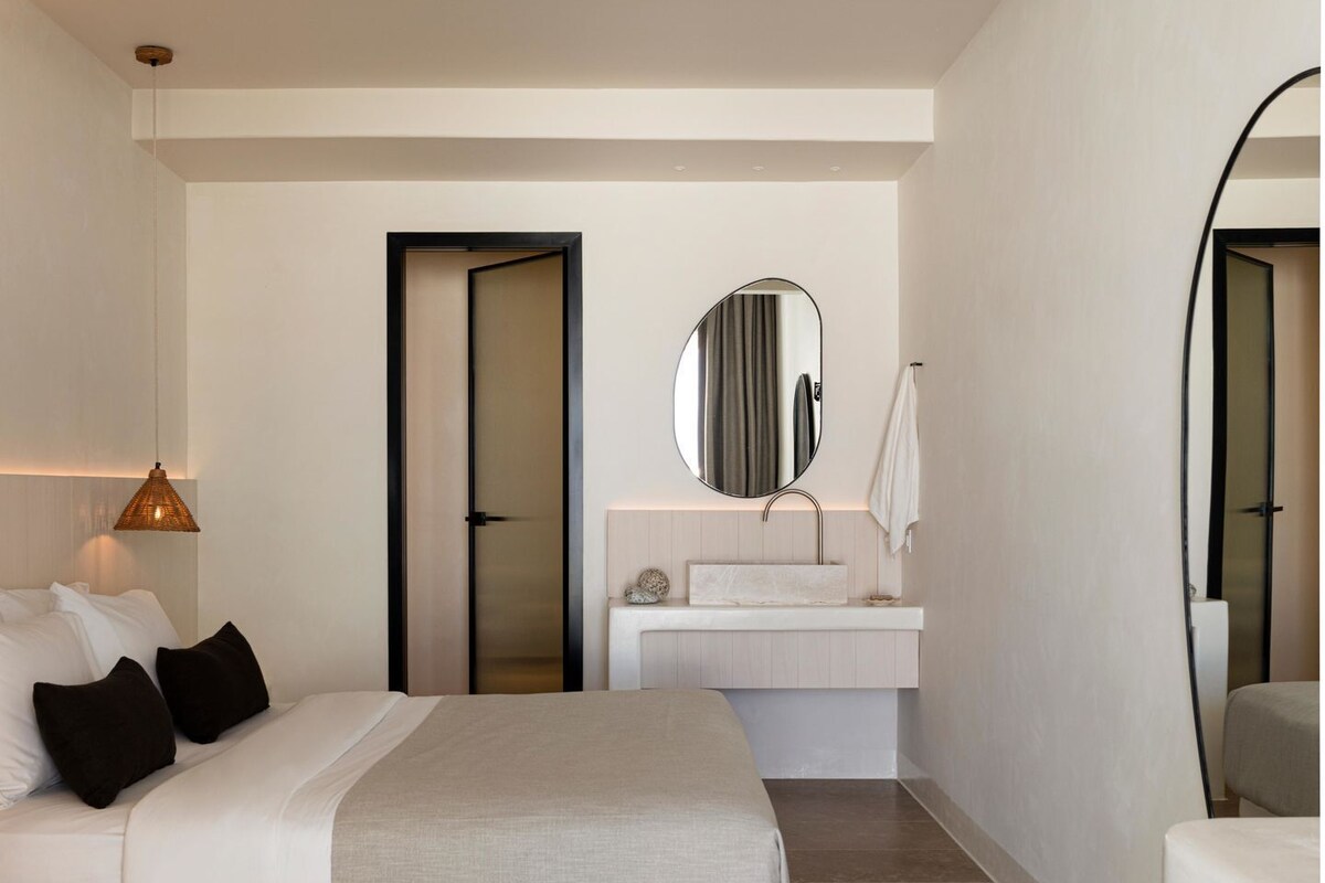 A modern hotel room with a bed, a bedside table, a mirror, and a bathroom area with a sink and toilet.