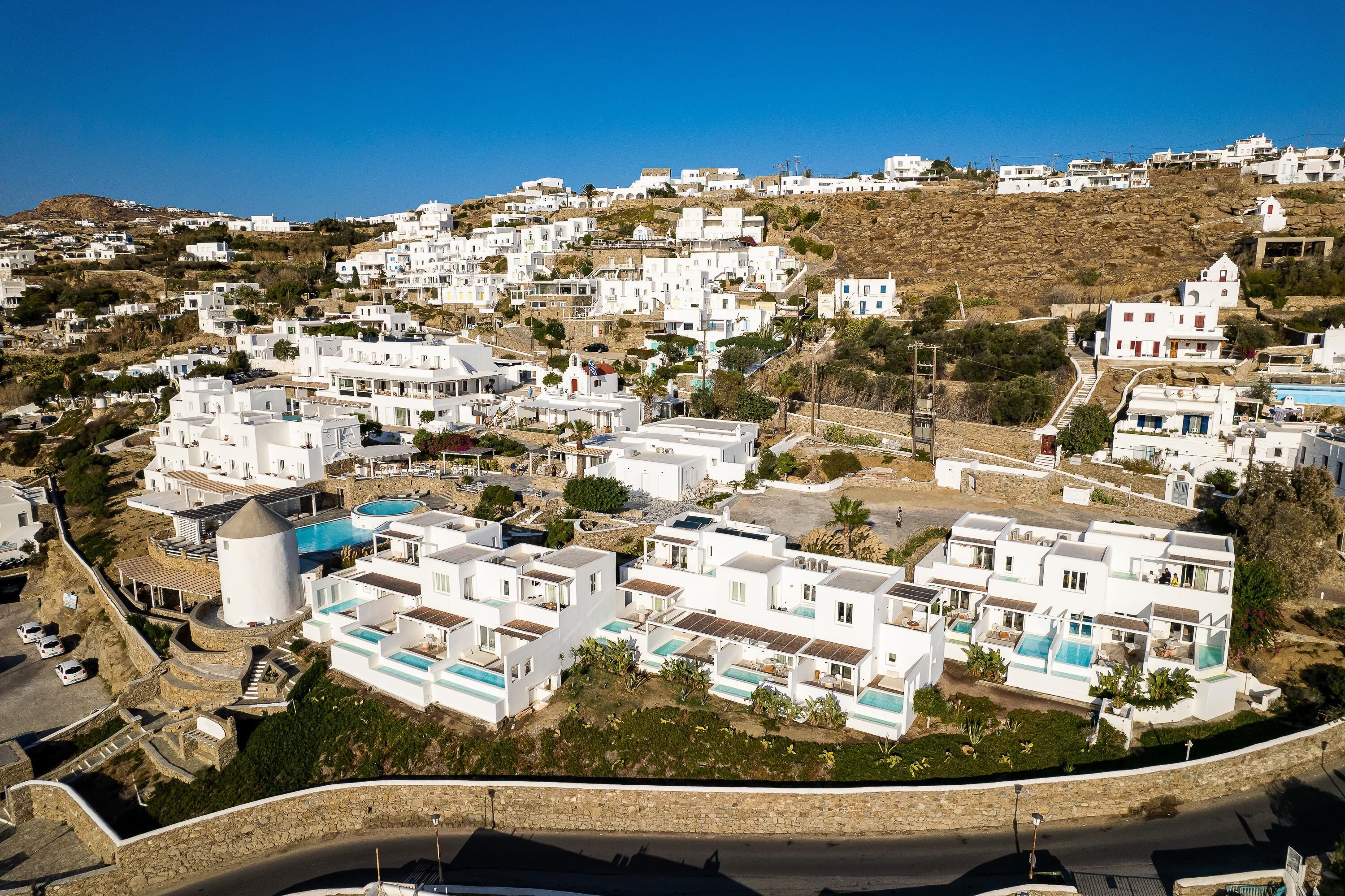 A coastal village with white buildings, a swimming pool, and a stone wall.